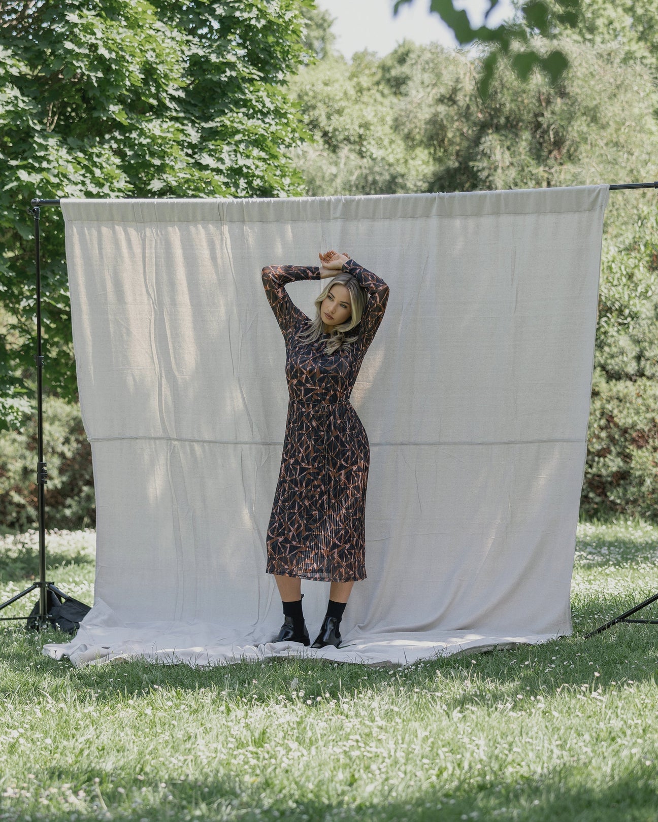 Woman in geometric-patterned dress posing outdoors with white backdrop, stylish knitwear fashion