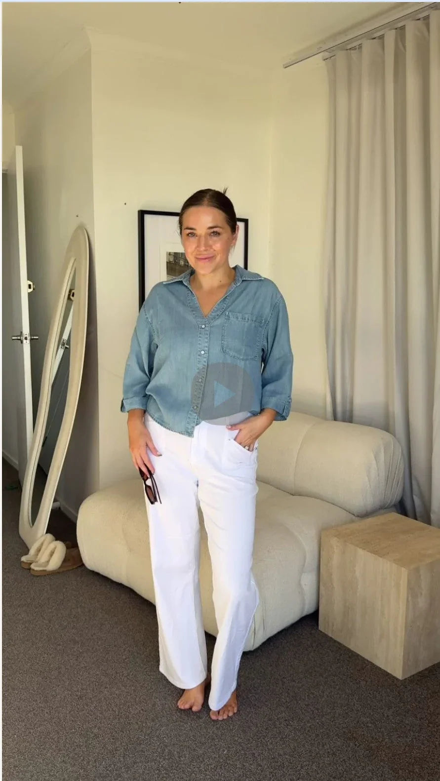 Woman wearing casual denim shirt and white pants in a modern living room