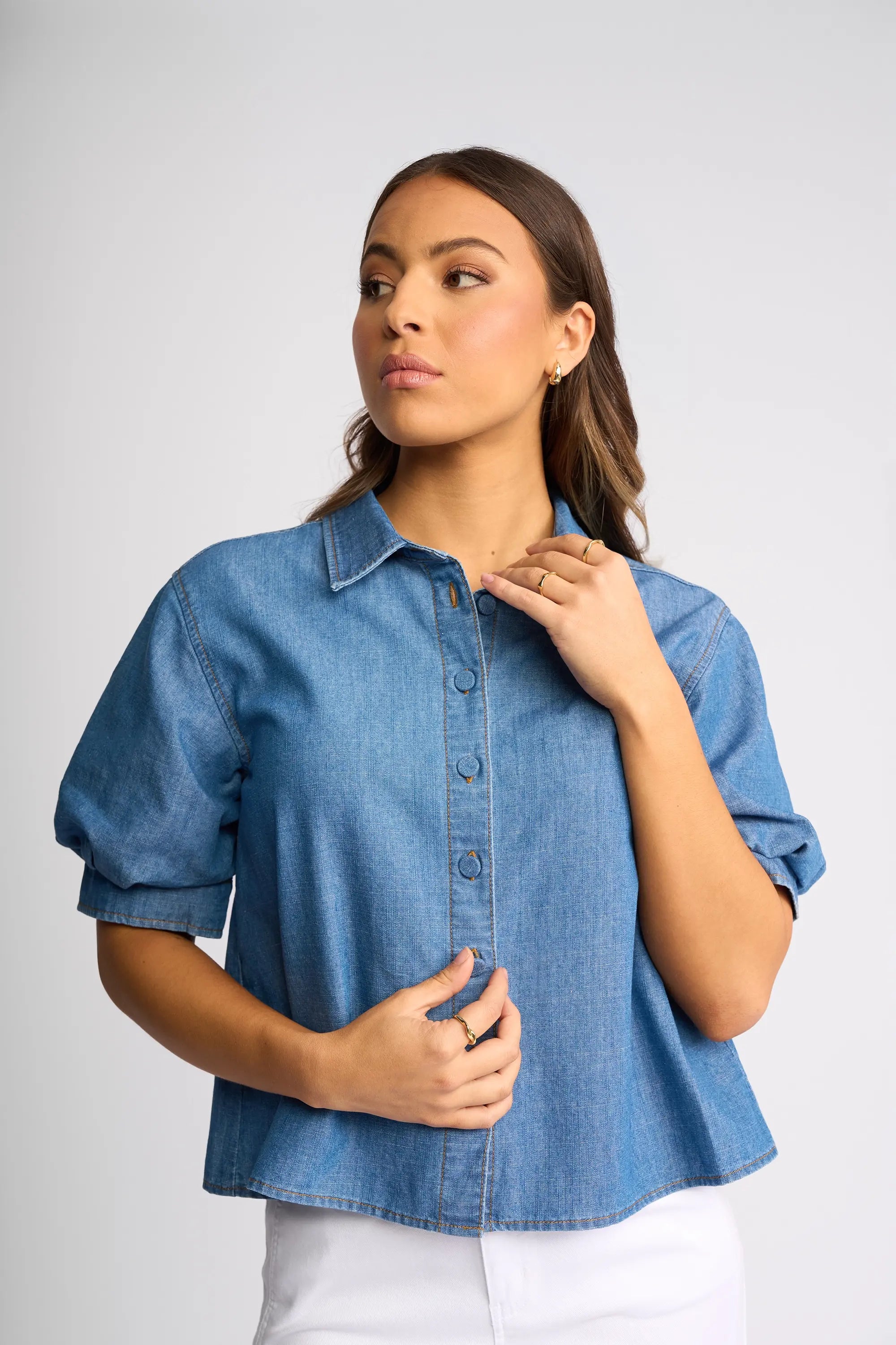 A person wearing a bright orange long-sleeve shirt with textured details and wide-leg blue jeans stands against a plain light background, looking slightly downward.