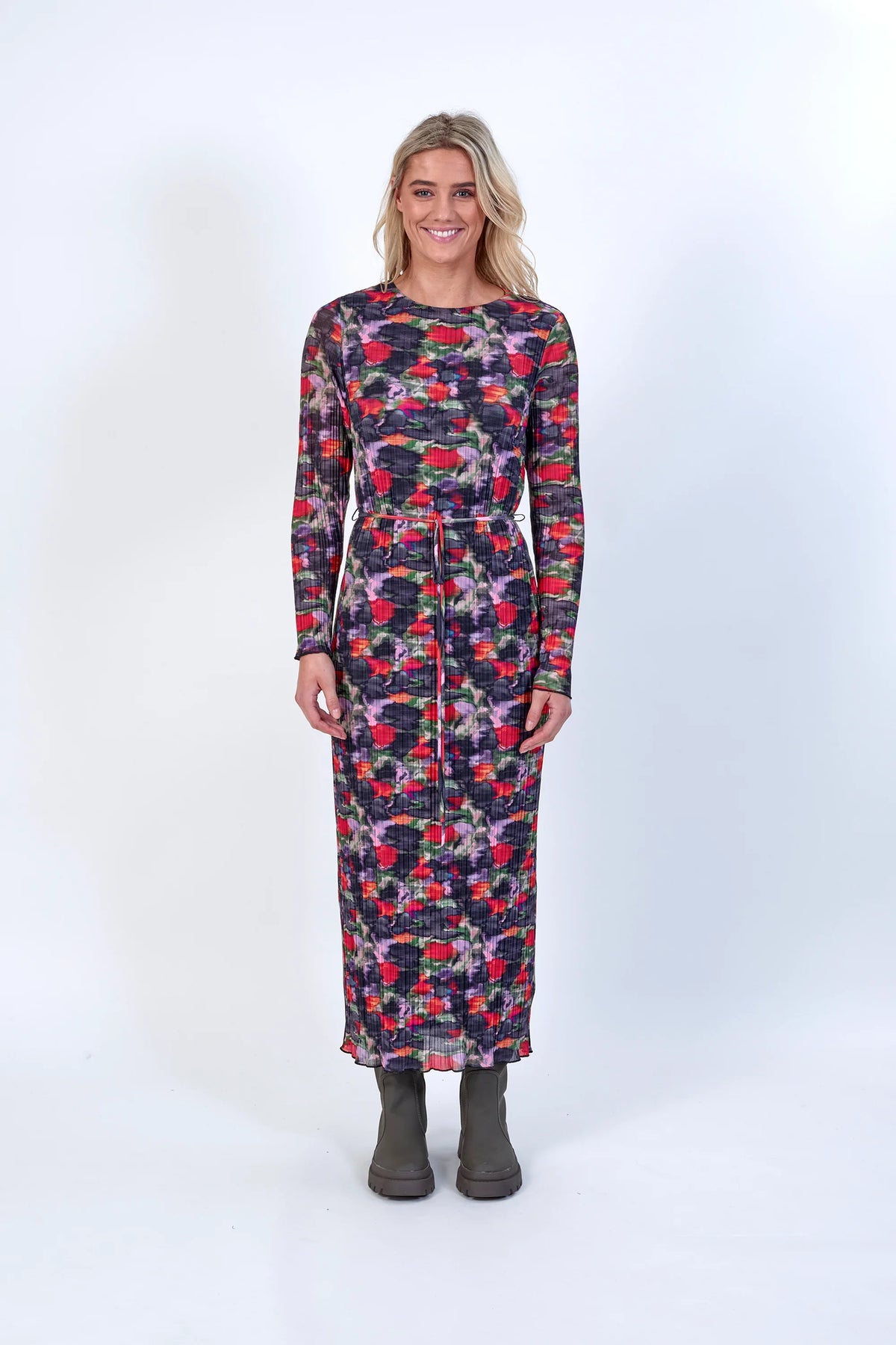 Woman wearing a long-sleeve abstract floral print dress with tie waist and boots, studio background