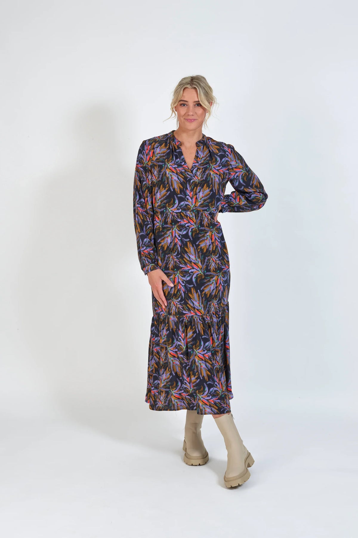 Woman in long-sleeve floral print midi dress with neutral boots, standing against white background