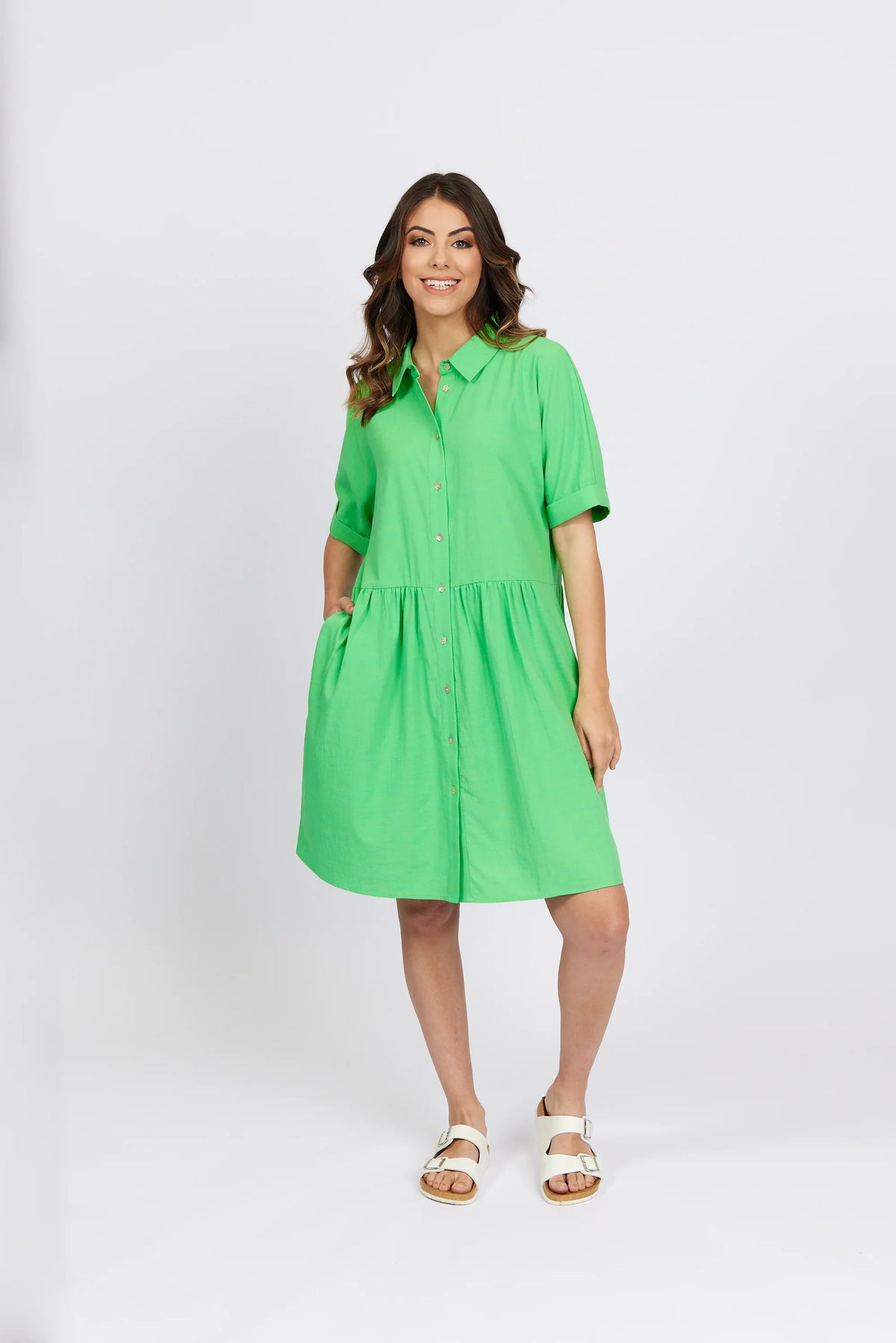 Woman wearing a bright green short sleeve button-up cocoon dress with collar and side pockets