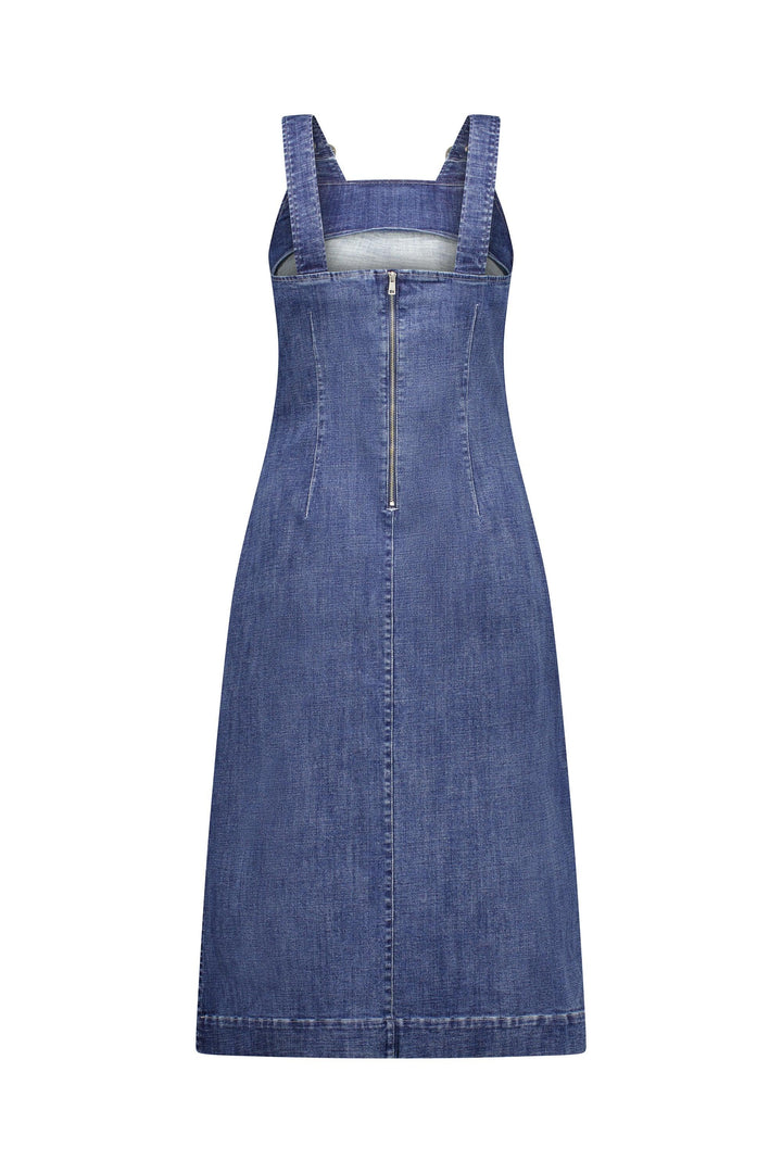The Academy Dress - Mid Wash by Knewe Label is a sleeveless blue A-line dress with wide pinafore straps, front zipper, and visible seam details. Made from stretch denim with a slightly faded wash.