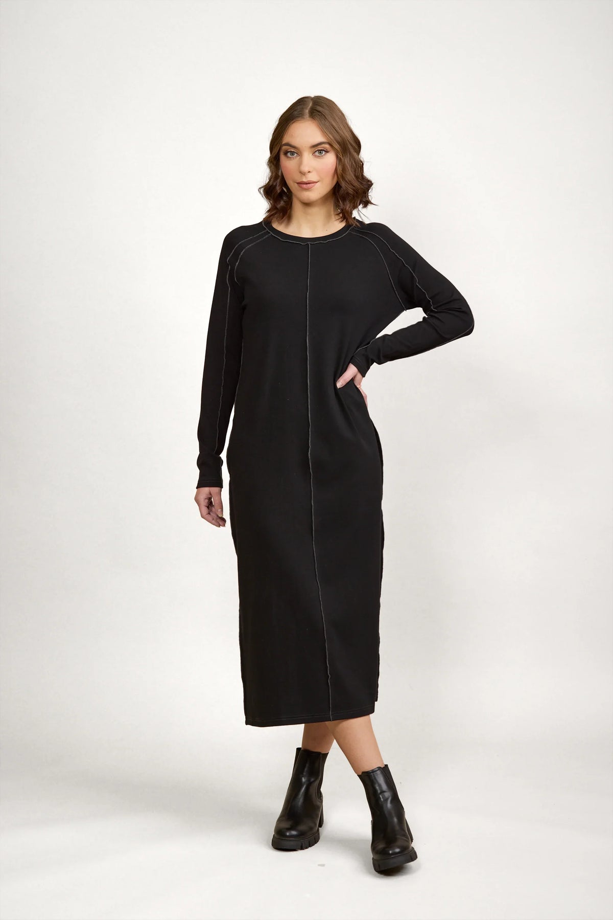 Woman wearing long sleeve black midi dress with contrast stitching and black ankle boots