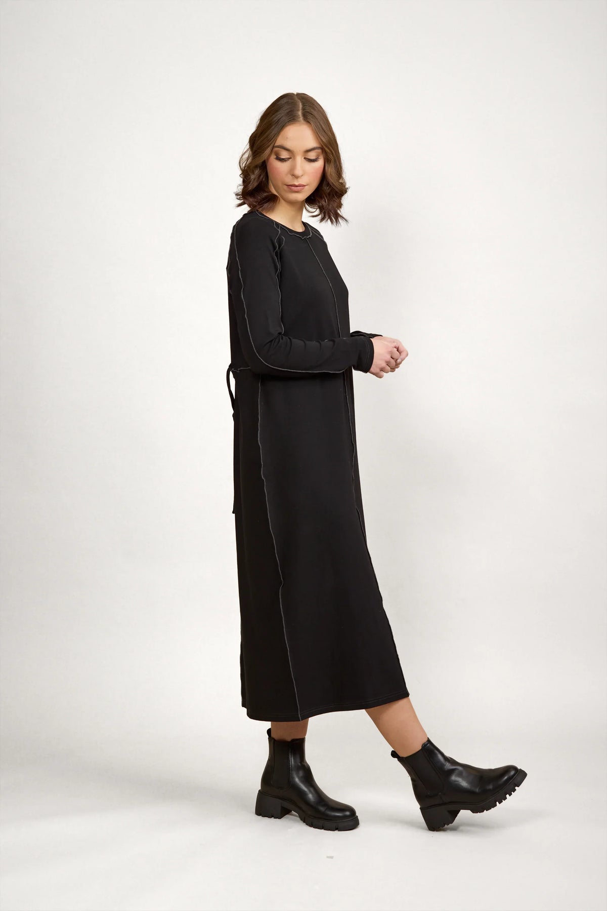 Woman wearing a long sleeve black midi dress with contrast stitching and ankle boots
