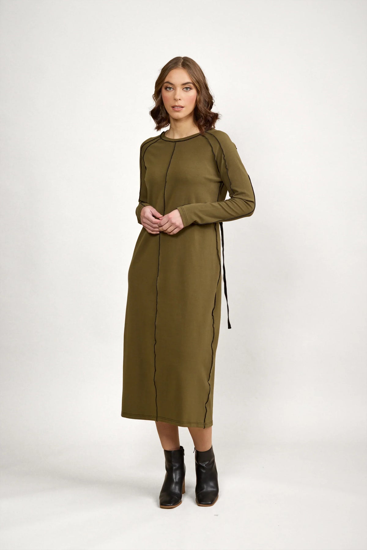 Woman in olive green long sleeve midi dress with black seam detail, standing indoors