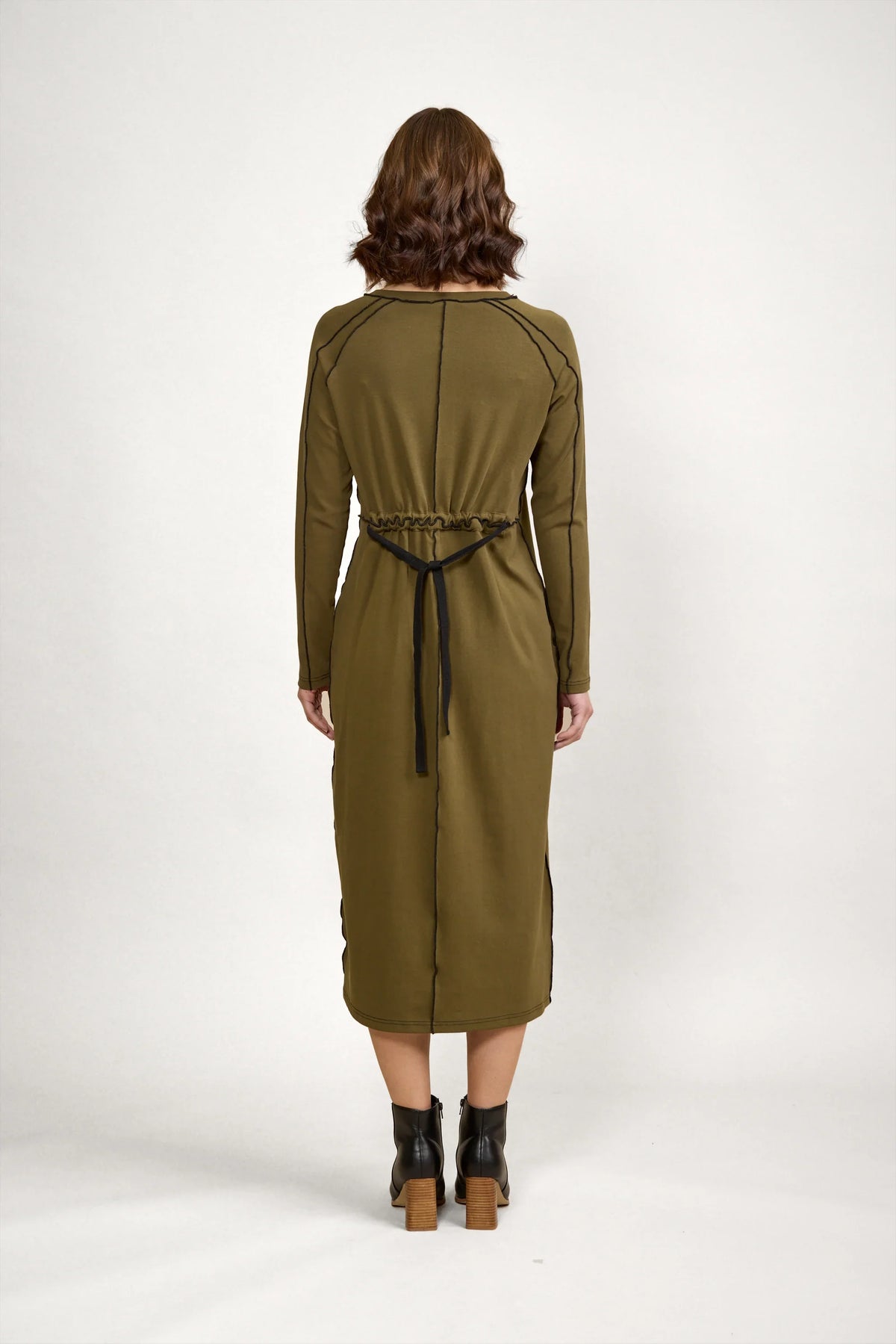Back view of woman wearing olive green long sleeve midi dress with black tie waist
