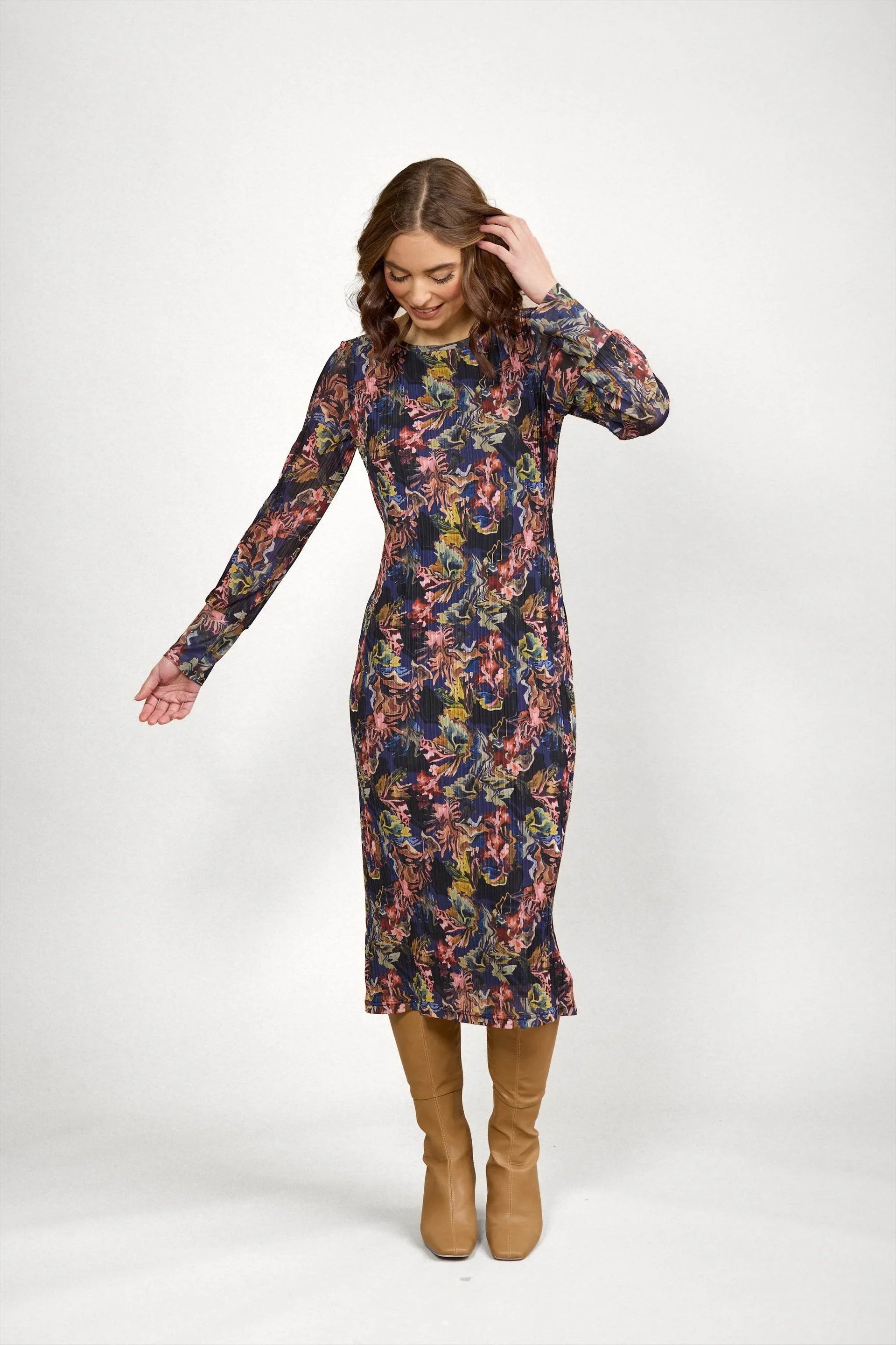 Woman wearing a long sleeve floral midi dress with tan knee-high boots on a plain background
