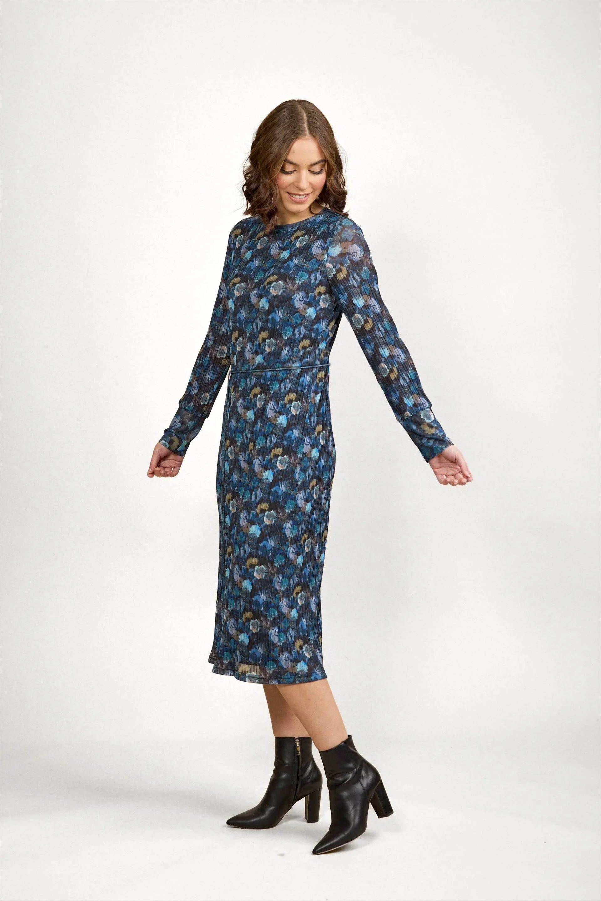 Woman wearing a long-sleeve blue floral midi dress with black ankle boots, studio background.
