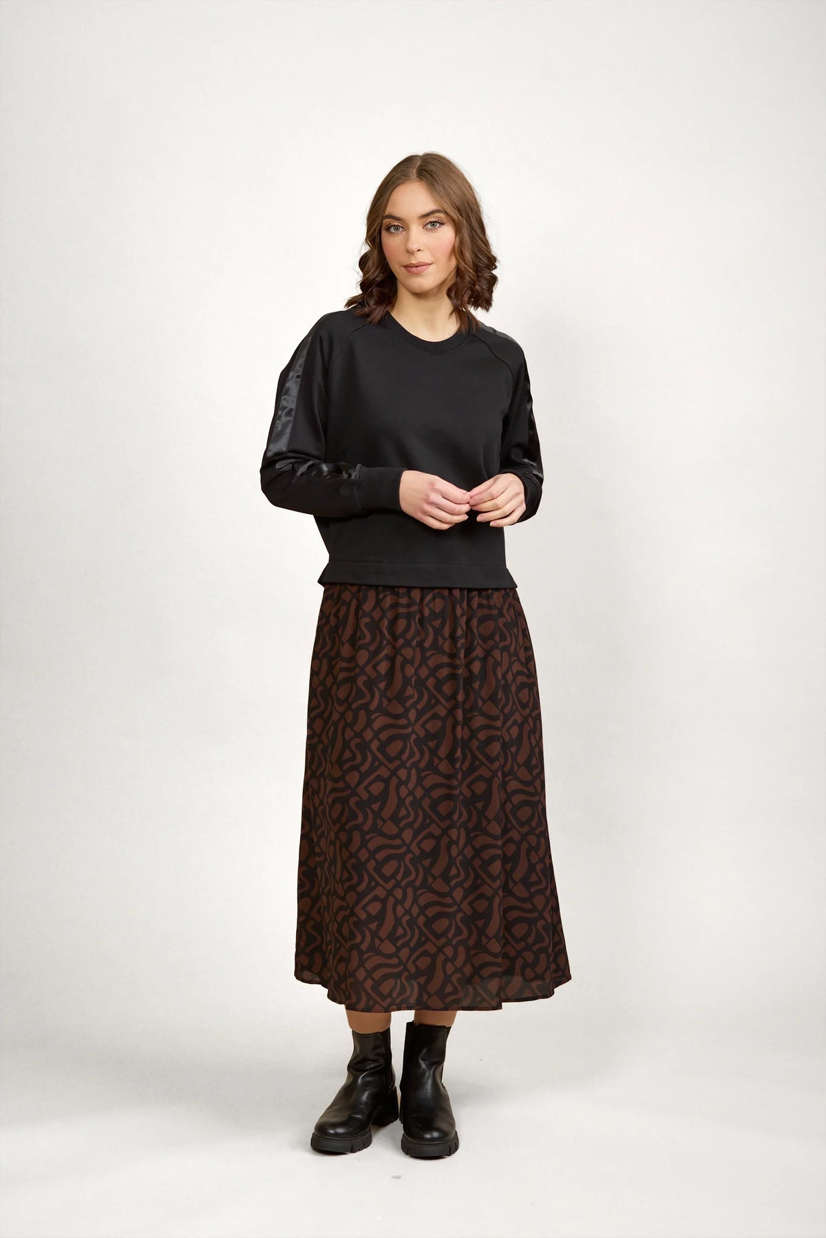 Woman wearing a black long-sleeve top and mocha brown patterned midi skirt with black boots