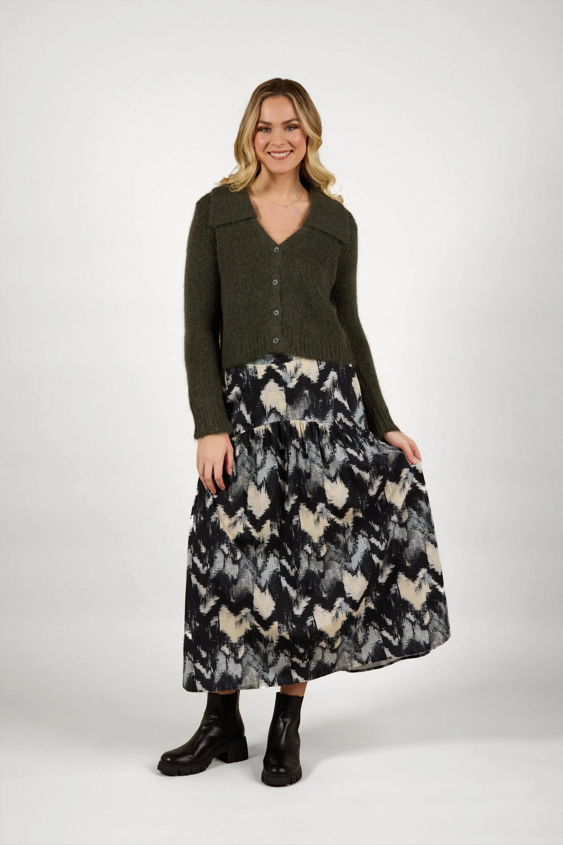 Woman in olive knit cardigan and abstract print maxi skirt with black boots