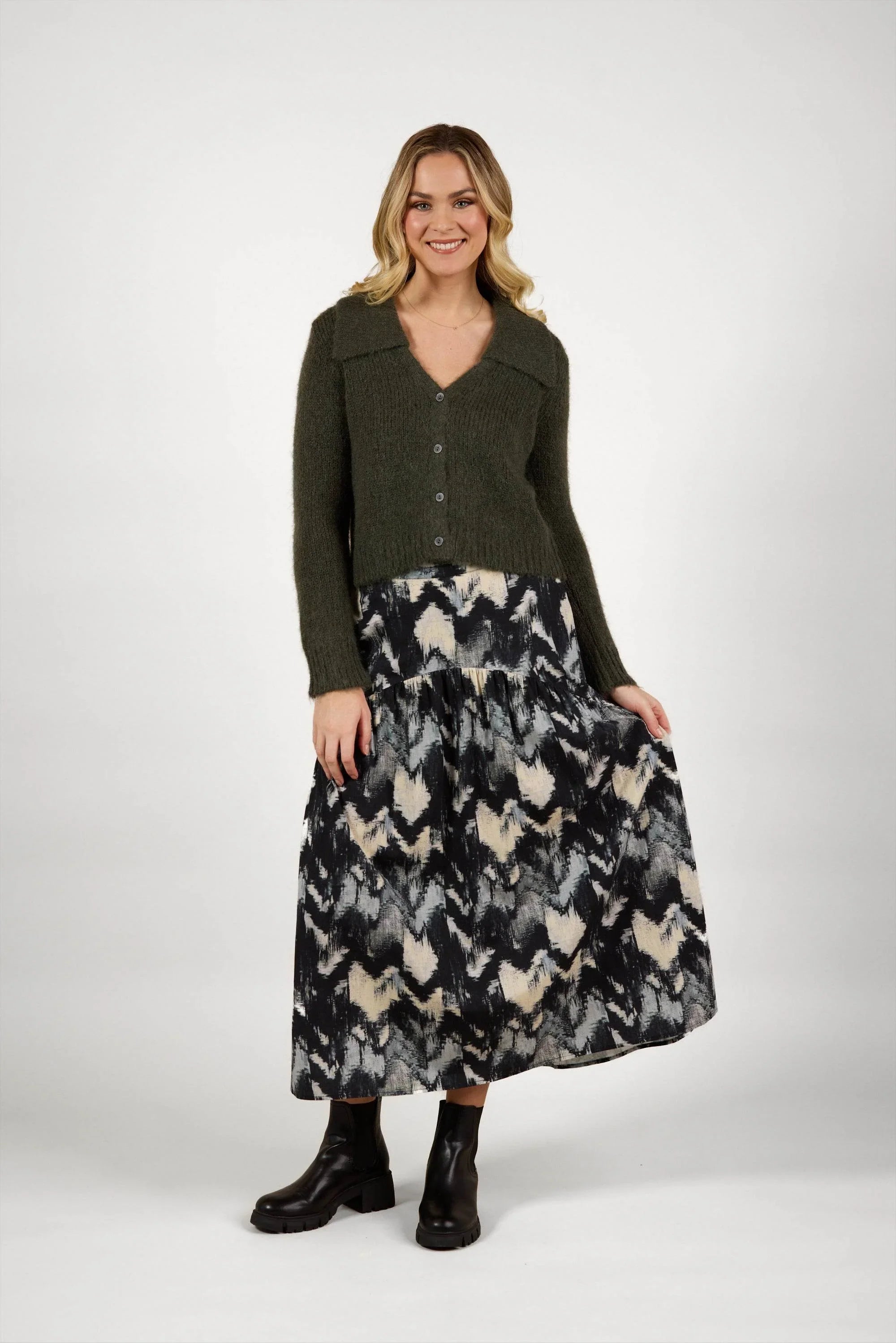 Woman in olive knit cardigan and abstract print maxi skirt with black boots