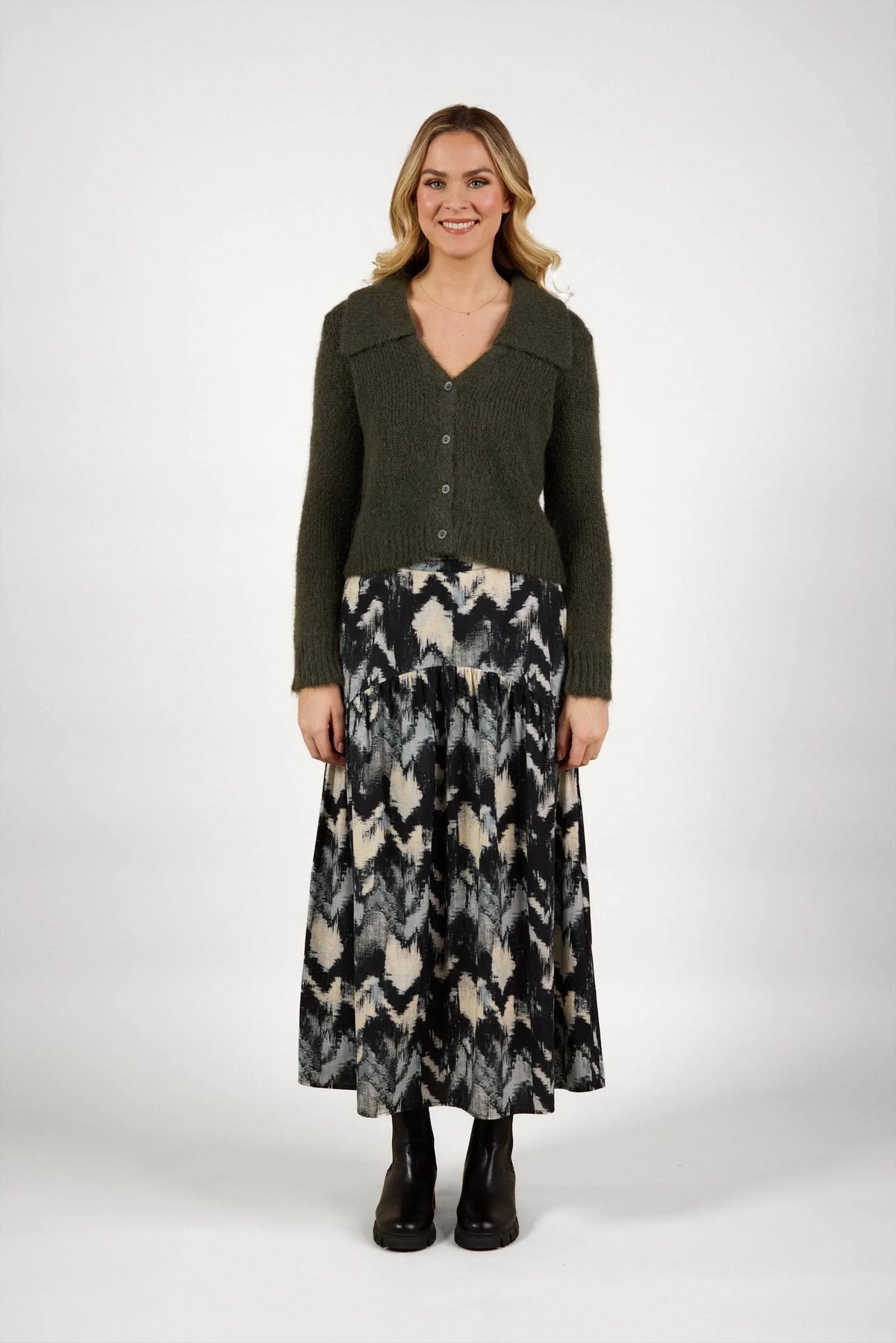 Woman wearing an olive green knit cardigan with a patterned black and cream maxi skirt
