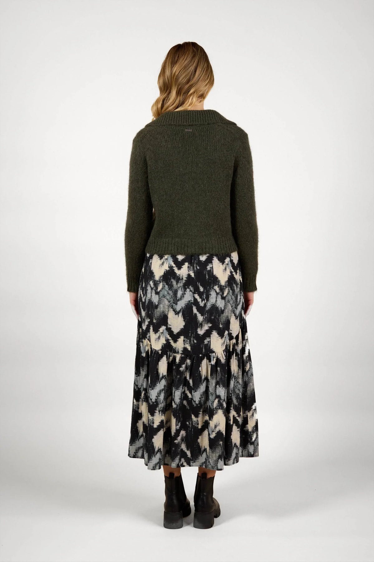 Woman wearing dark green knit sweater and abstract print midi skirt, back view