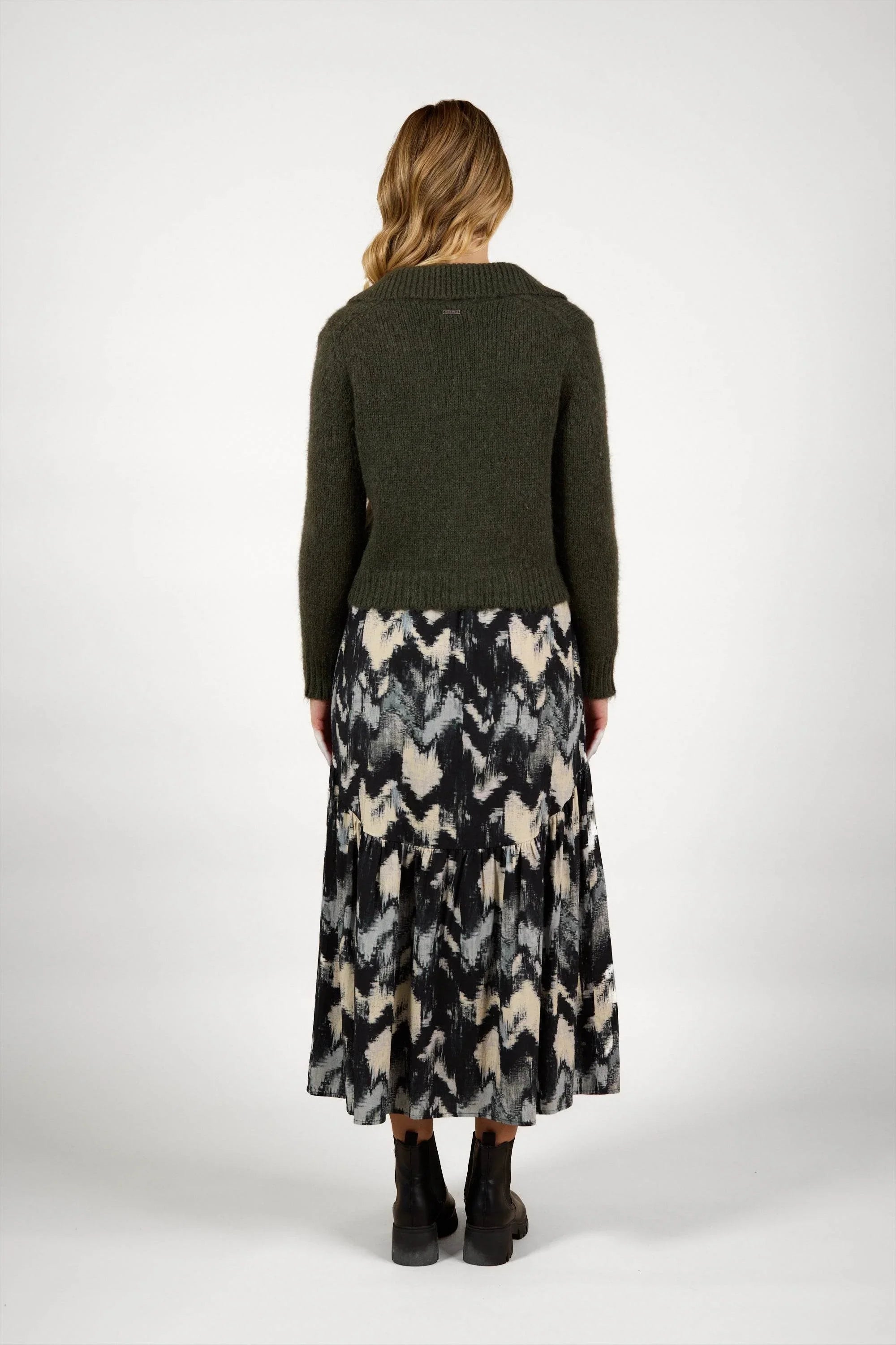 Woman wearing dark green knit sweater and abstract print midi skirt, back view