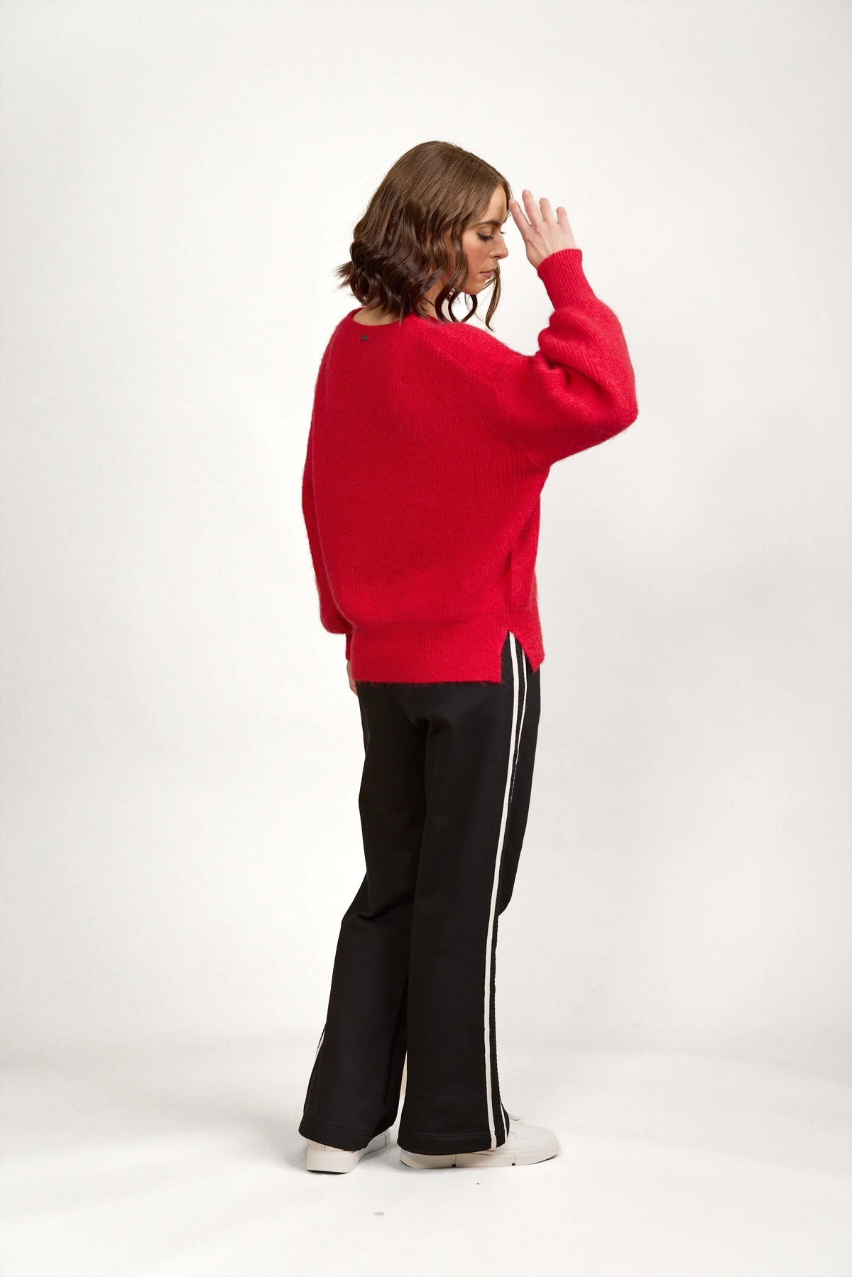 Woman in a red knit sweater and black pants with white side stripes, posing indoors