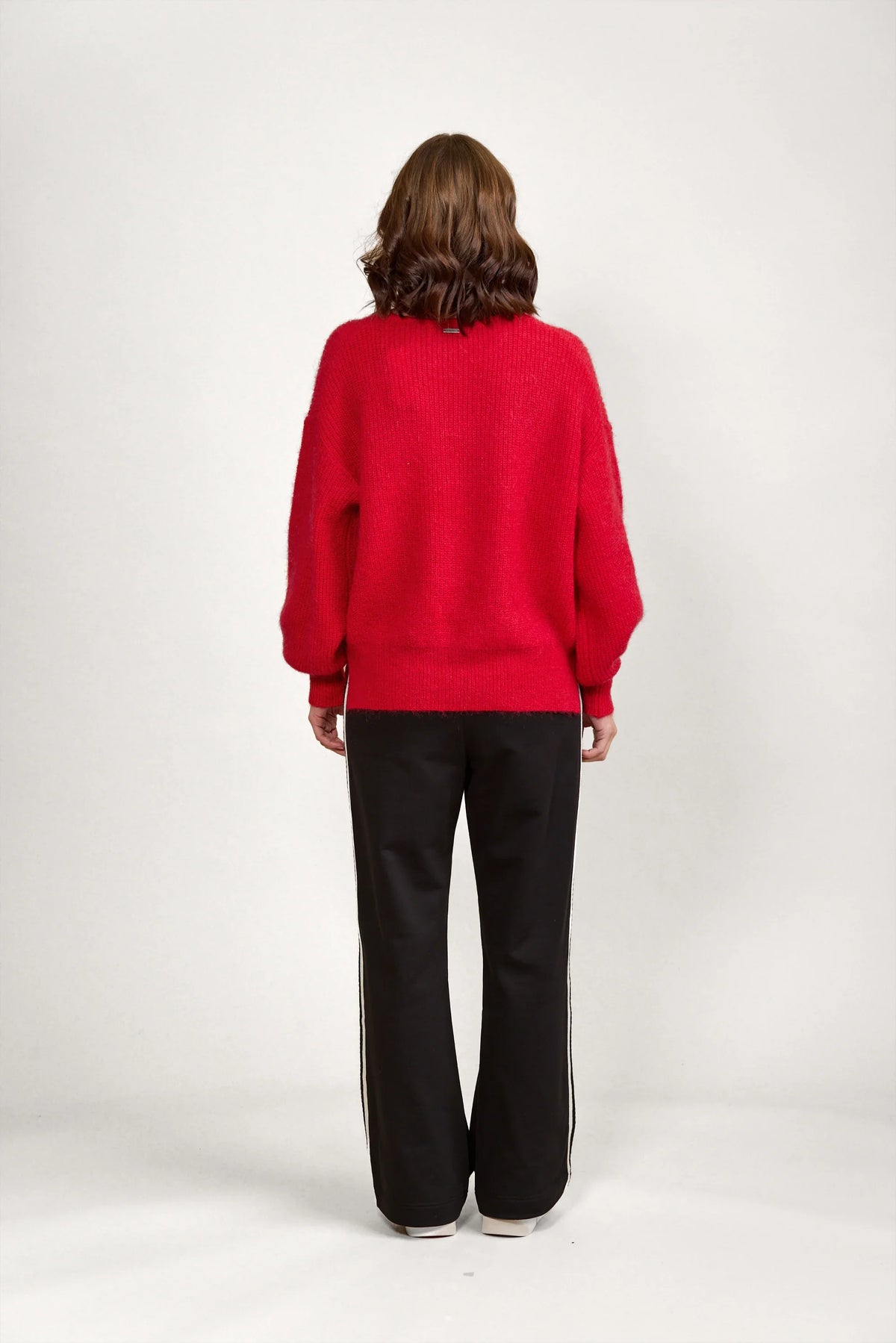 Woman wearing a red knit sweater and black pants, back view, minimalist studio setting