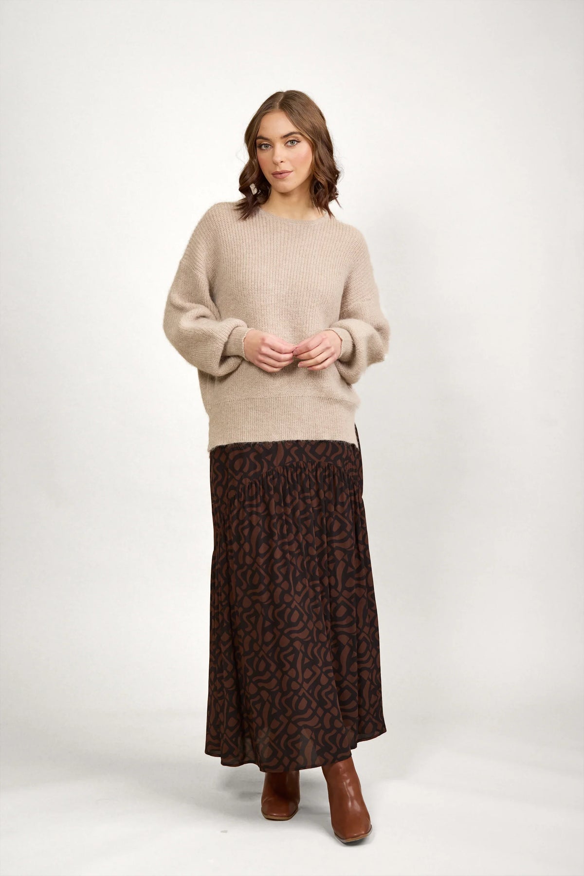 Woman wearing an oatmeal knit sweater with a patterned brown maxi skirt and brown boots