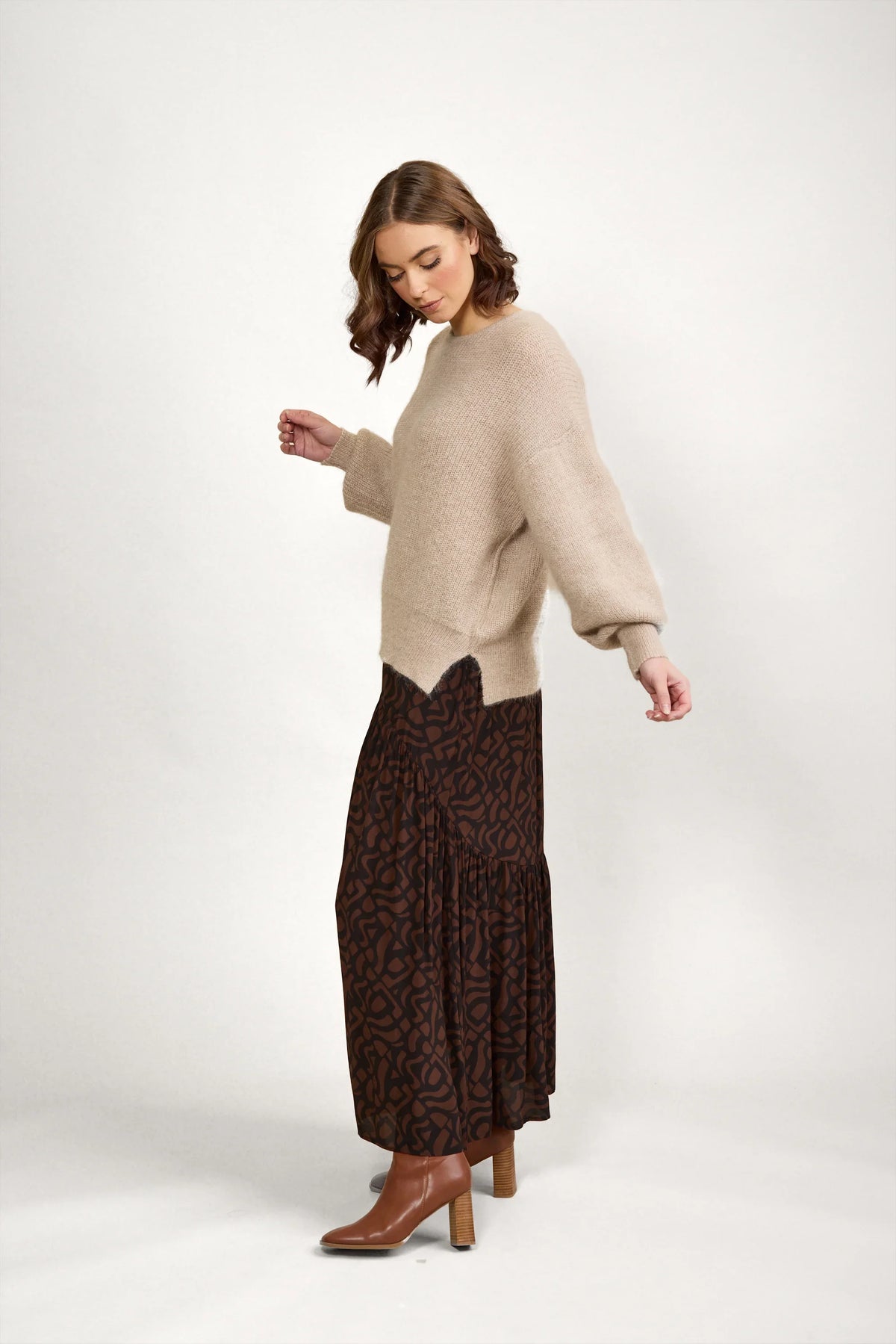 Woman in oatmeal knit sweater, brown printed maxi skirt, and tan ankle boots
