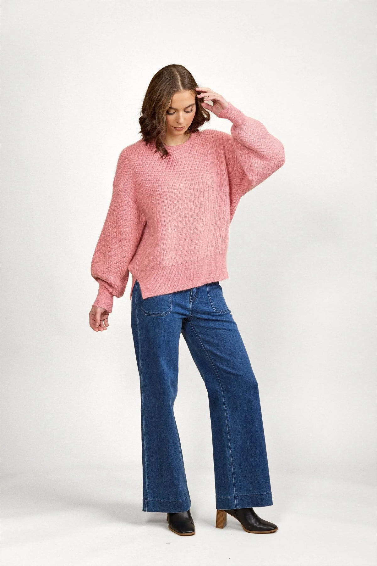 Woman wearing a loose pink knit sweater with wide-leg blue jeans and black boots