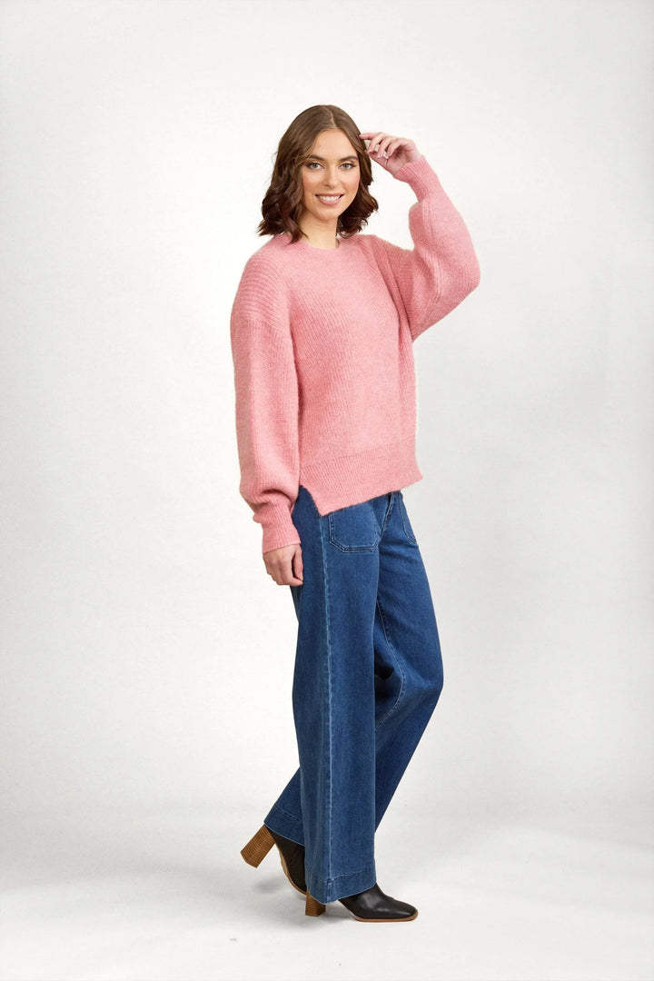 Woman wearing a pink knit sweater with wide-leg blue jeans and ankle boots, posing in studio