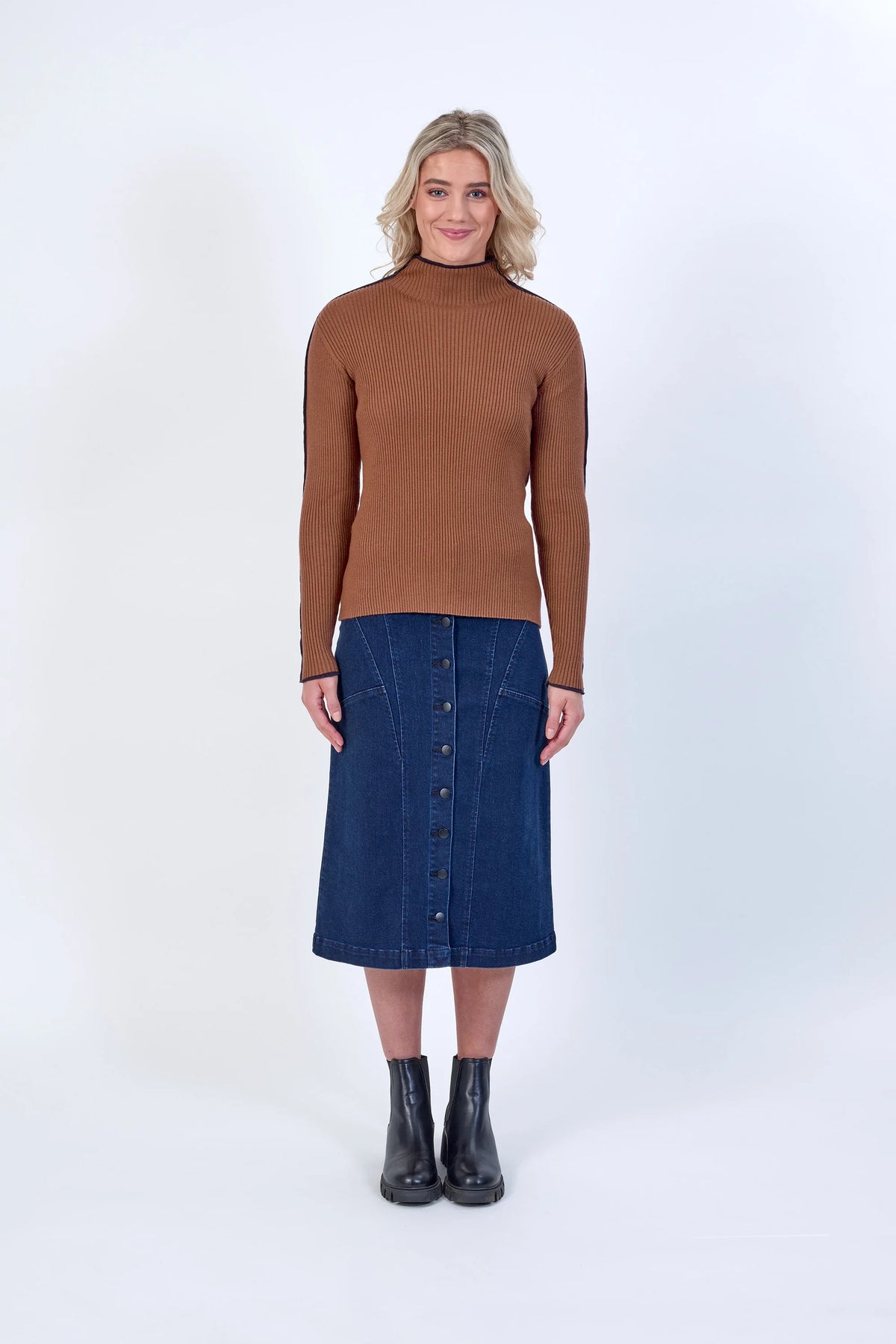 Woman in brown ribbed turtleneck sweater, blue denim button-front midi skirt, and black boots