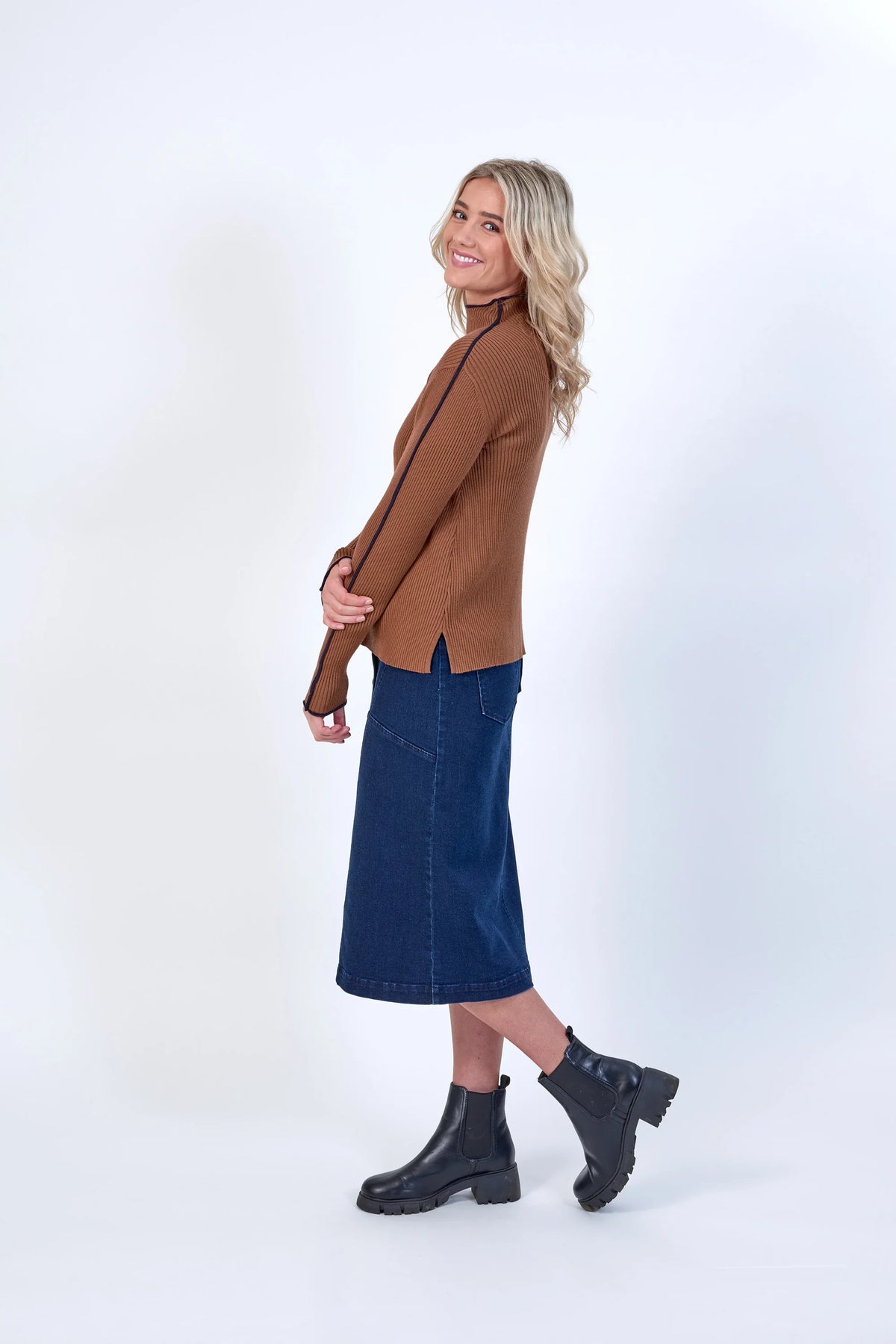 Woman in brown ribbed sweater, denim midi skirt, and black boots, showcasing stylish knitwear and label clothing.