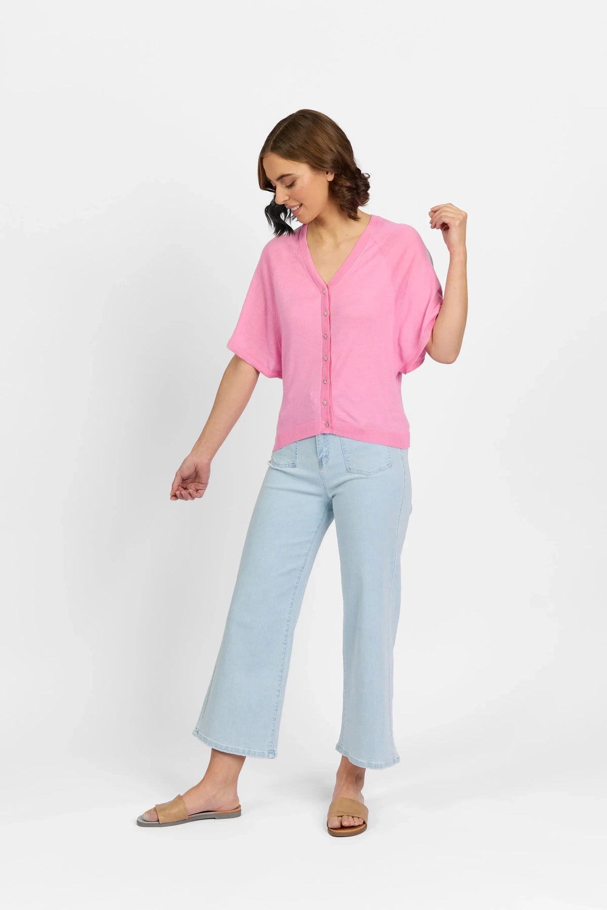 Woman wearing a pink button-front sweater and light blue wide-leg jeans on white background
