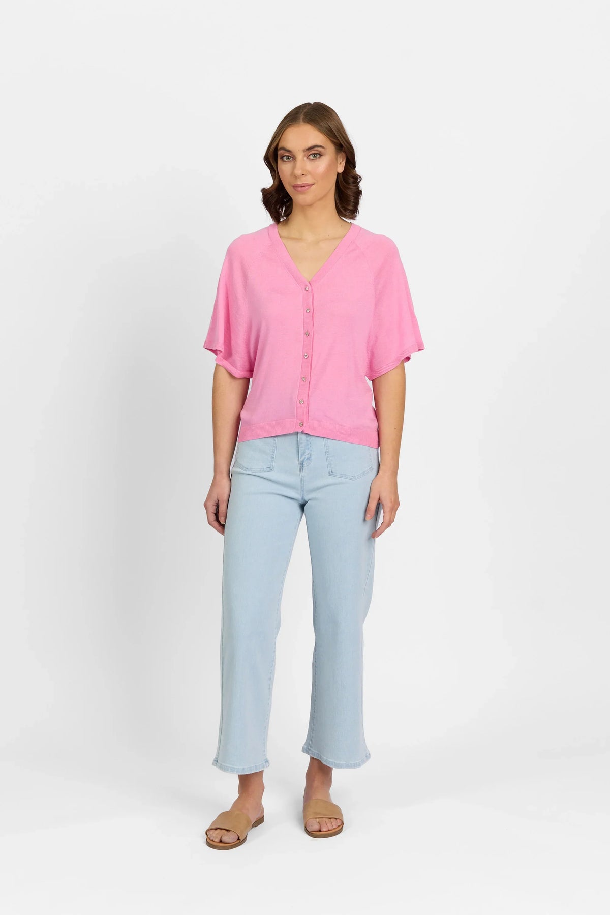 Woman wearing a pink button-up knit sweater, light wash jeans, and sandals on white background