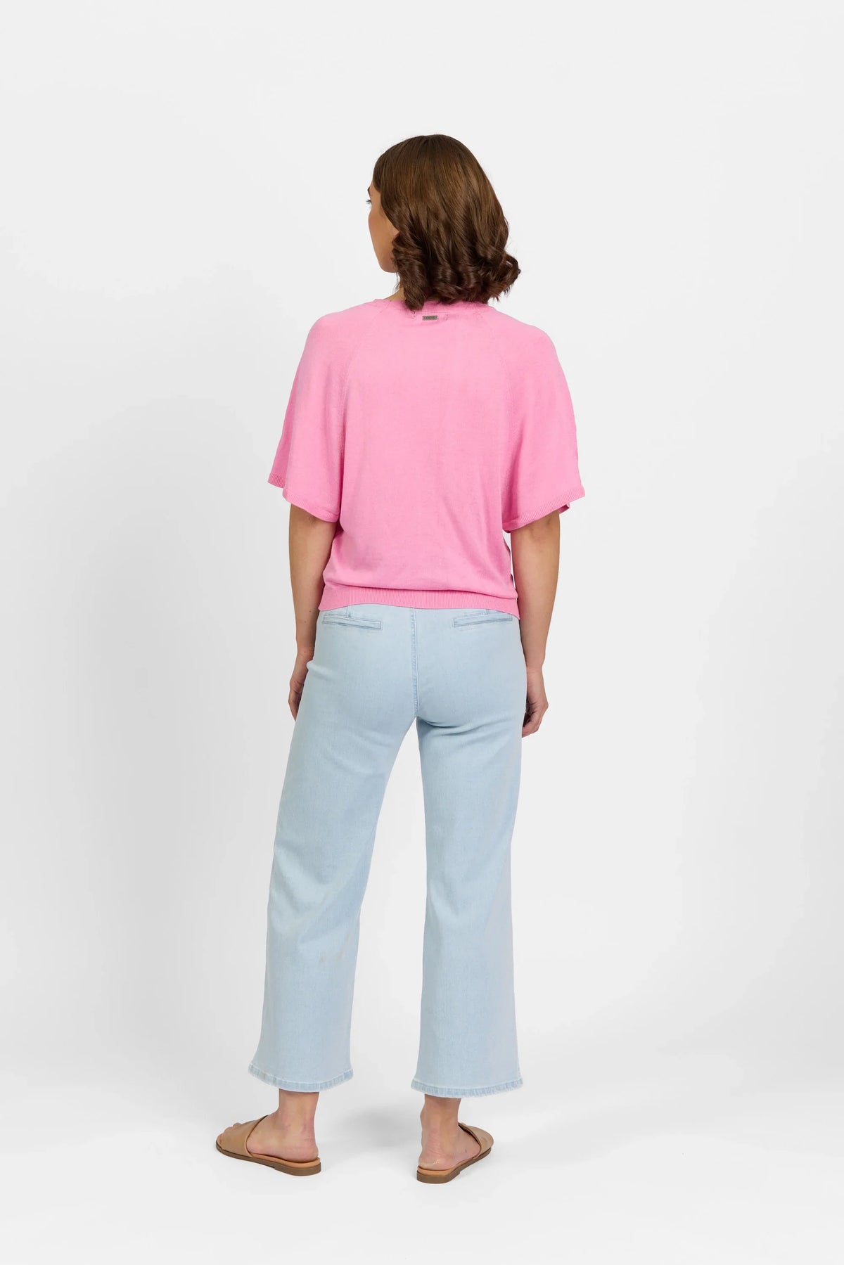 Woman wearing a pink sweater with short sleeves and light blue jeans, standing on white background