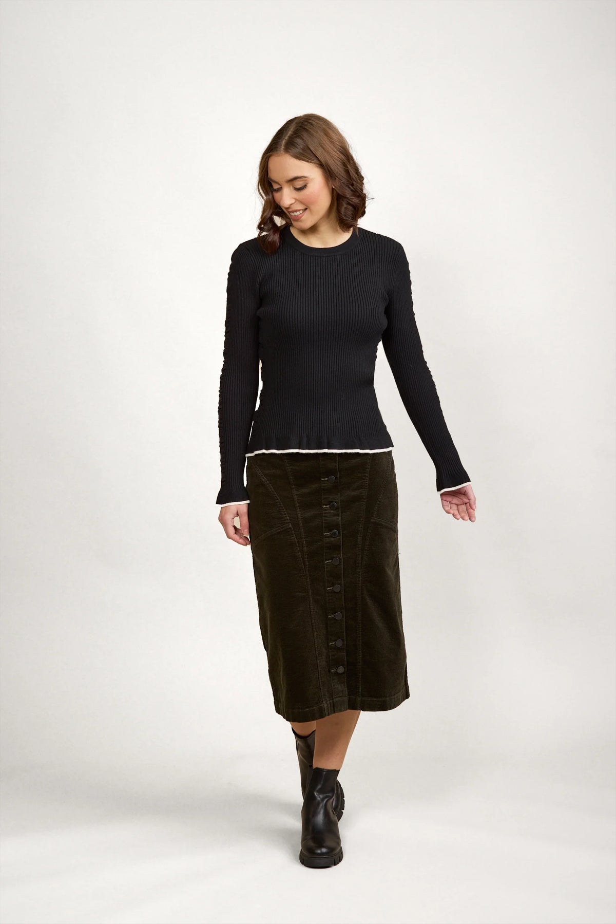 Woman wearing a black ribbed knit sweater with white trim, buttoned midi skirt, and black boots