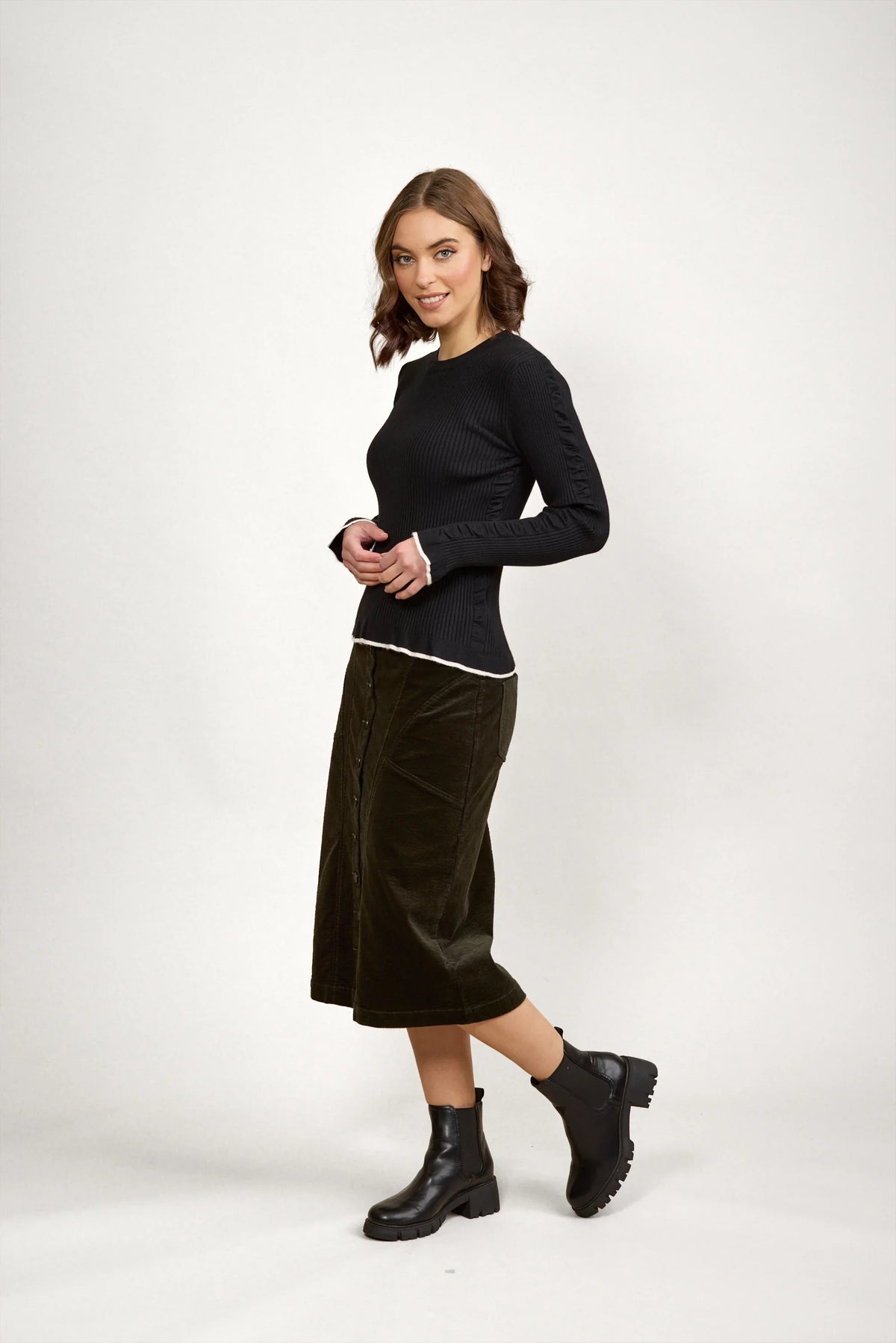 Woman wearing a fitted black knit sweater, midi skirt, and black ankle boots
