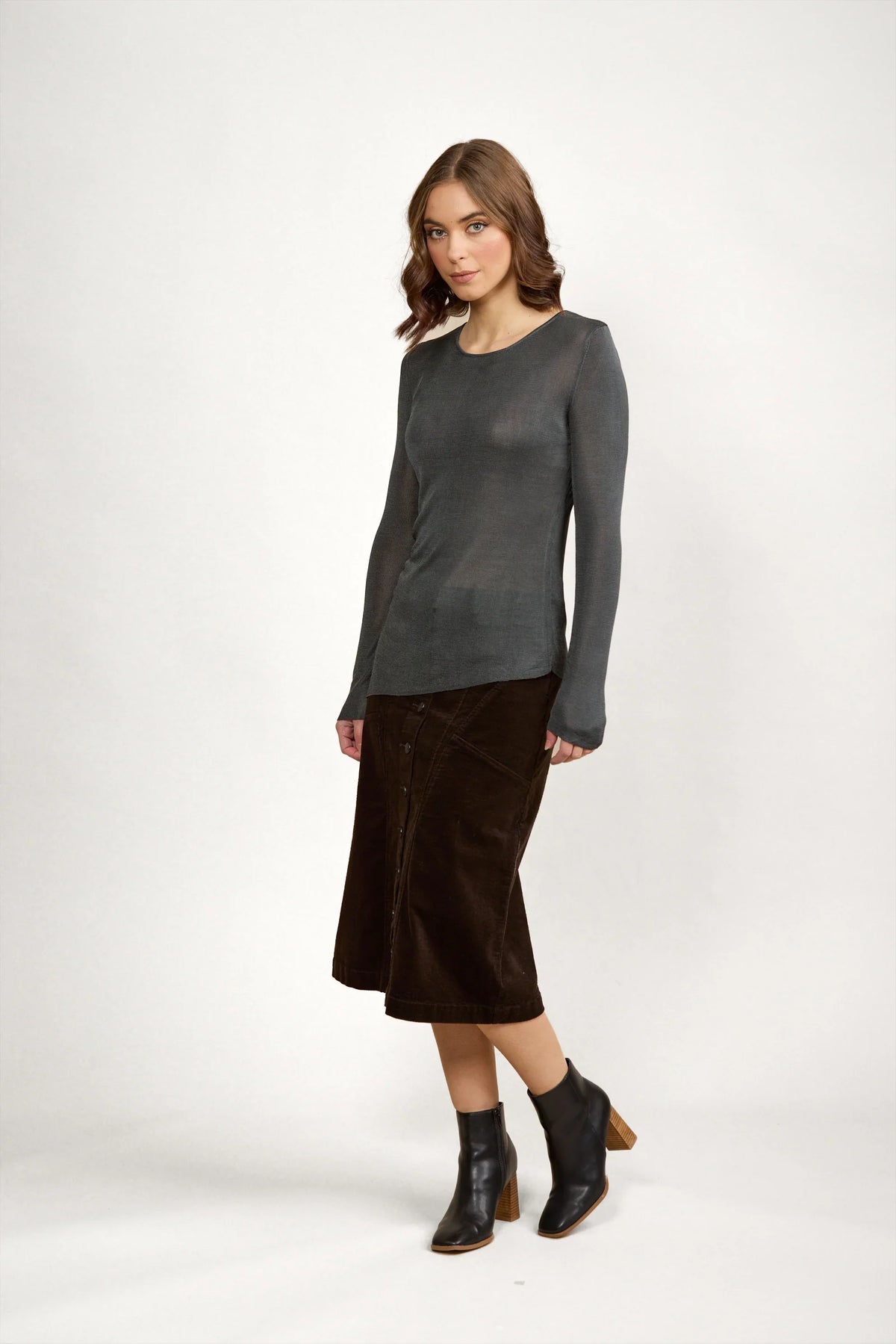 Woman wearing long sleeve grey knit sweater, brown midi skirt, and black ankle boots