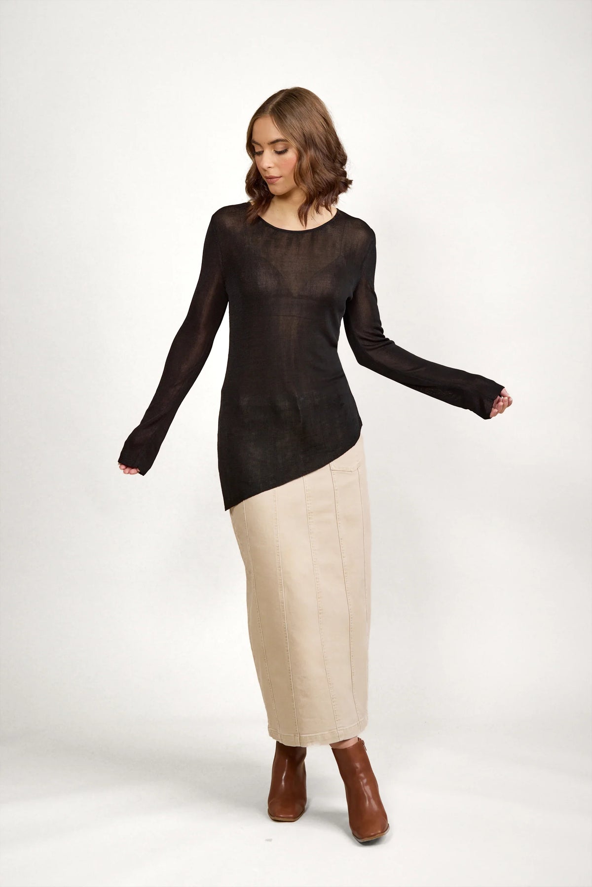Woman wearing black sheer knit sweater, beige maxi skirt, and brown ankle boots