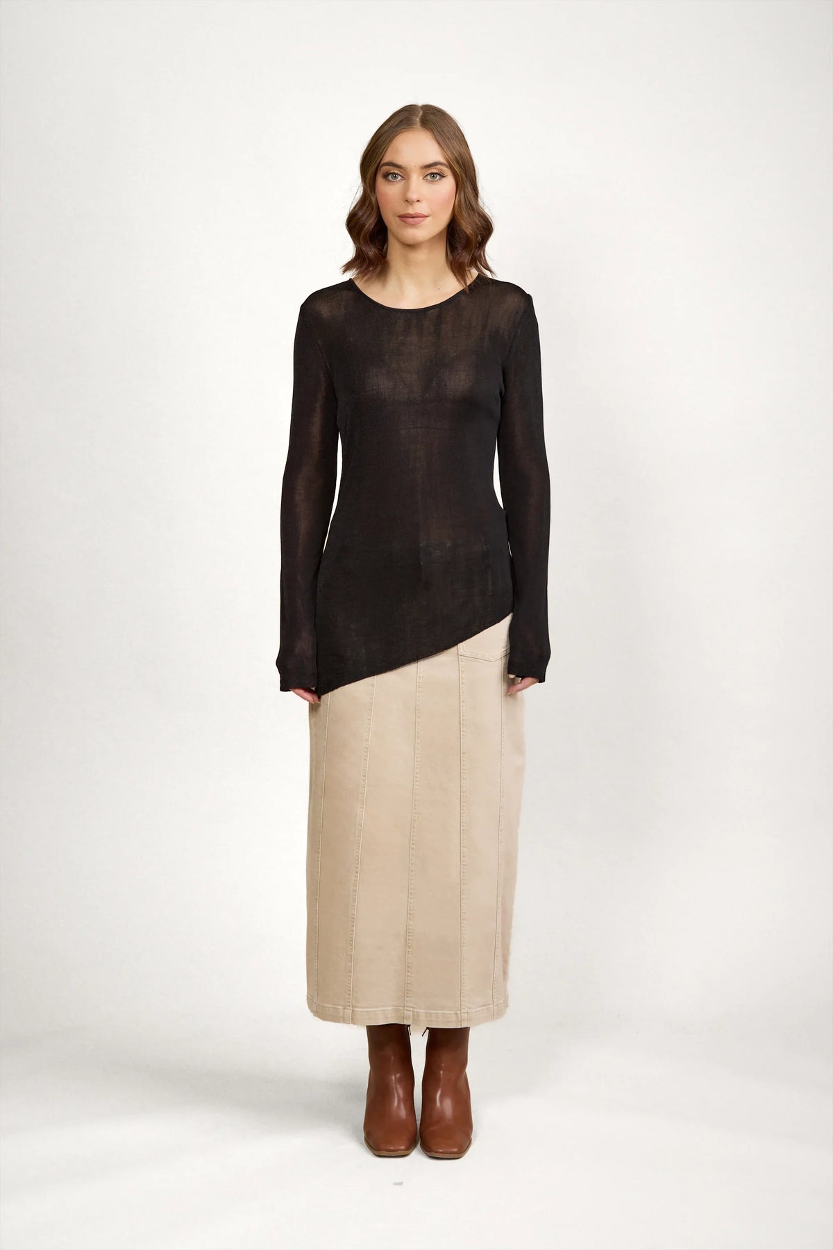 Woman wearing black sheer long sleeve sweater with beige midi skirt and brown boots