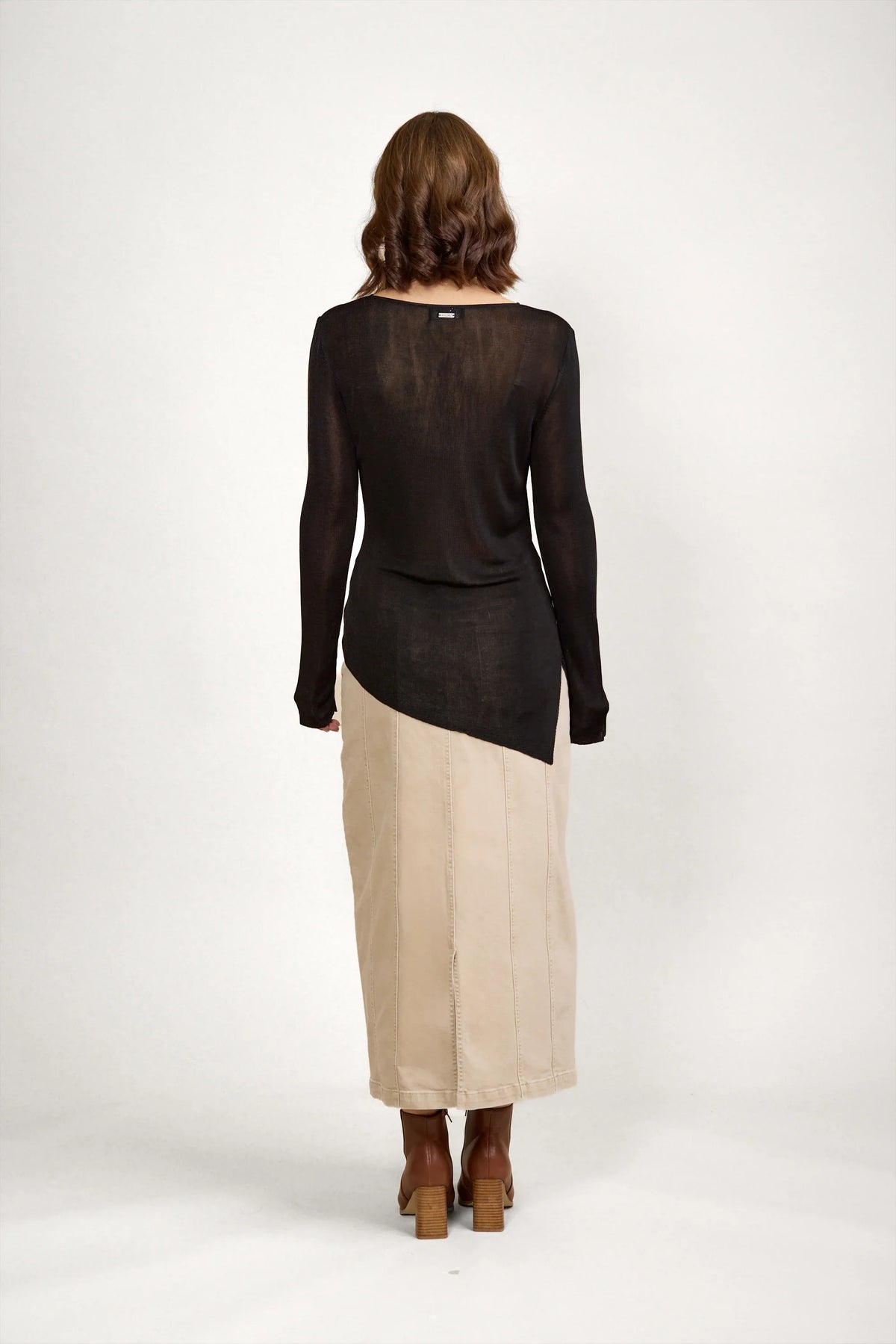 Woman wearing black long sleeve sweater and beige maxi skirt, back view, neutral background