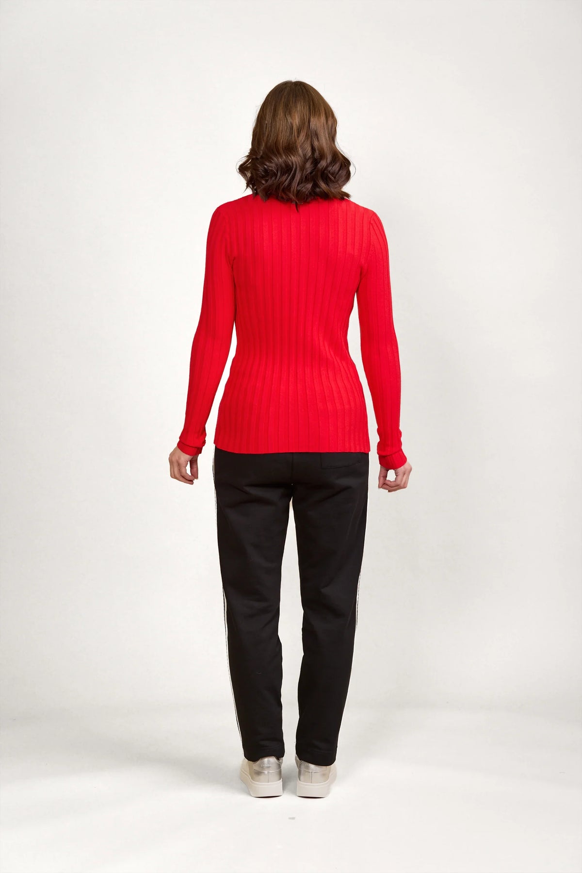 Woman wearing fitted red ribbed sweater and black pants, back view, studio background