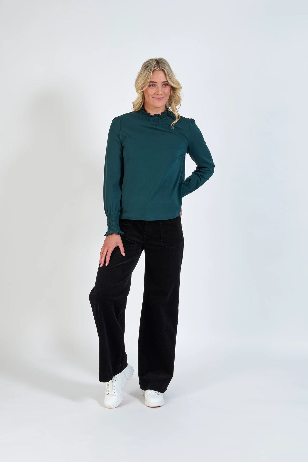 Woman wearing a dark green long sleeve blouse, black wide-leg pants, and white sneakers