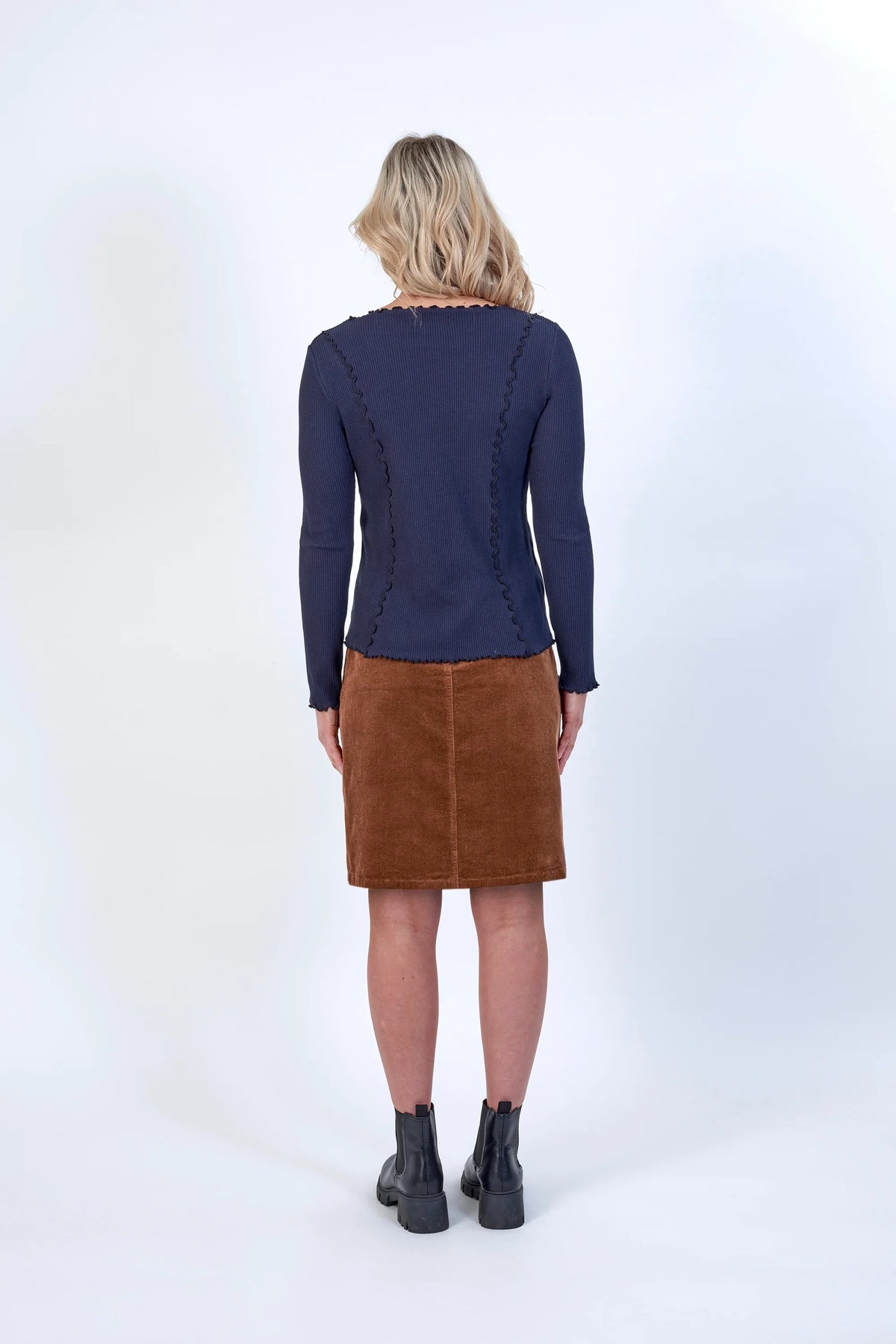 Woman wearing navy long sleeve top with wavy seams, brown corduroy skirt, black boots