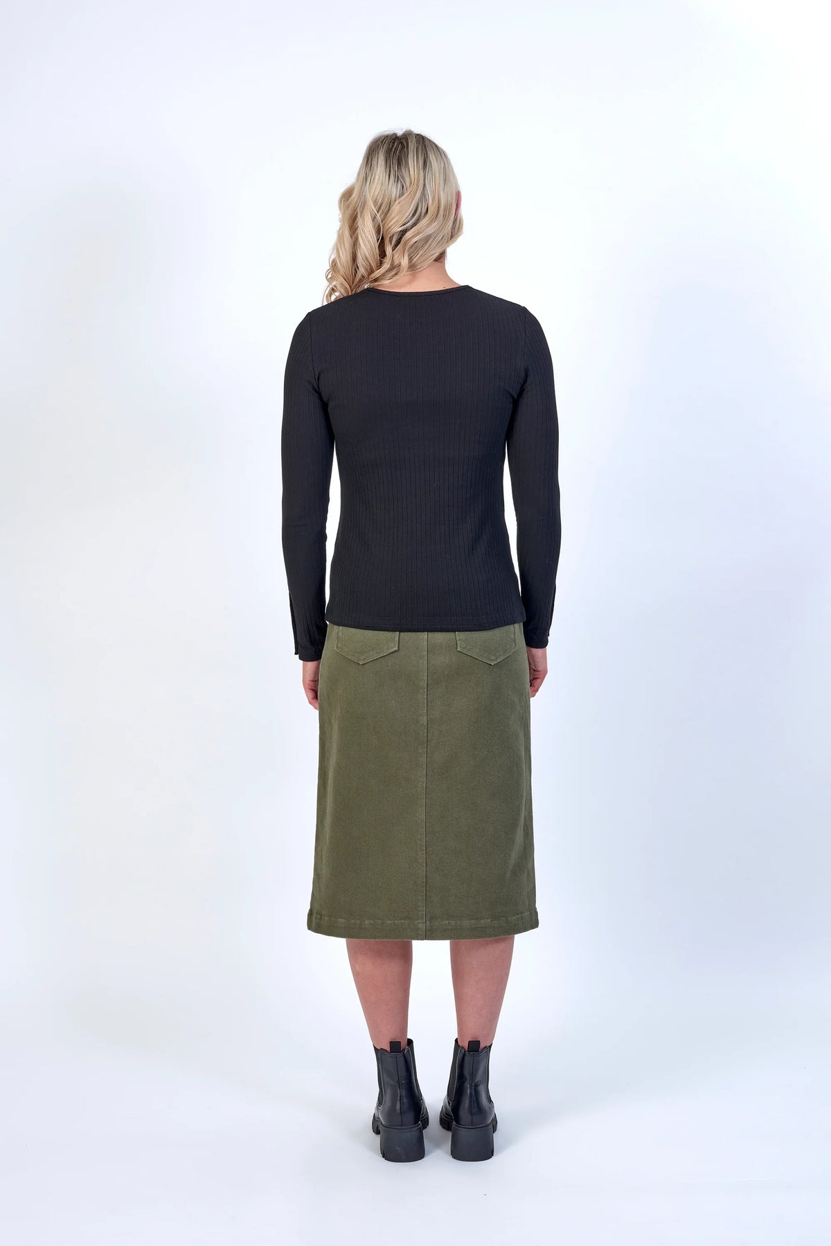 Woman in black long sleeve ribbed top and olive green midi skirt, back view