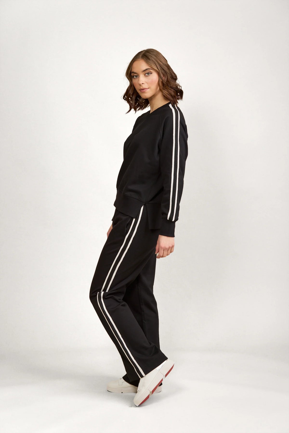 Woman wearing black knit tracksuit with white stripes, standing against plain background