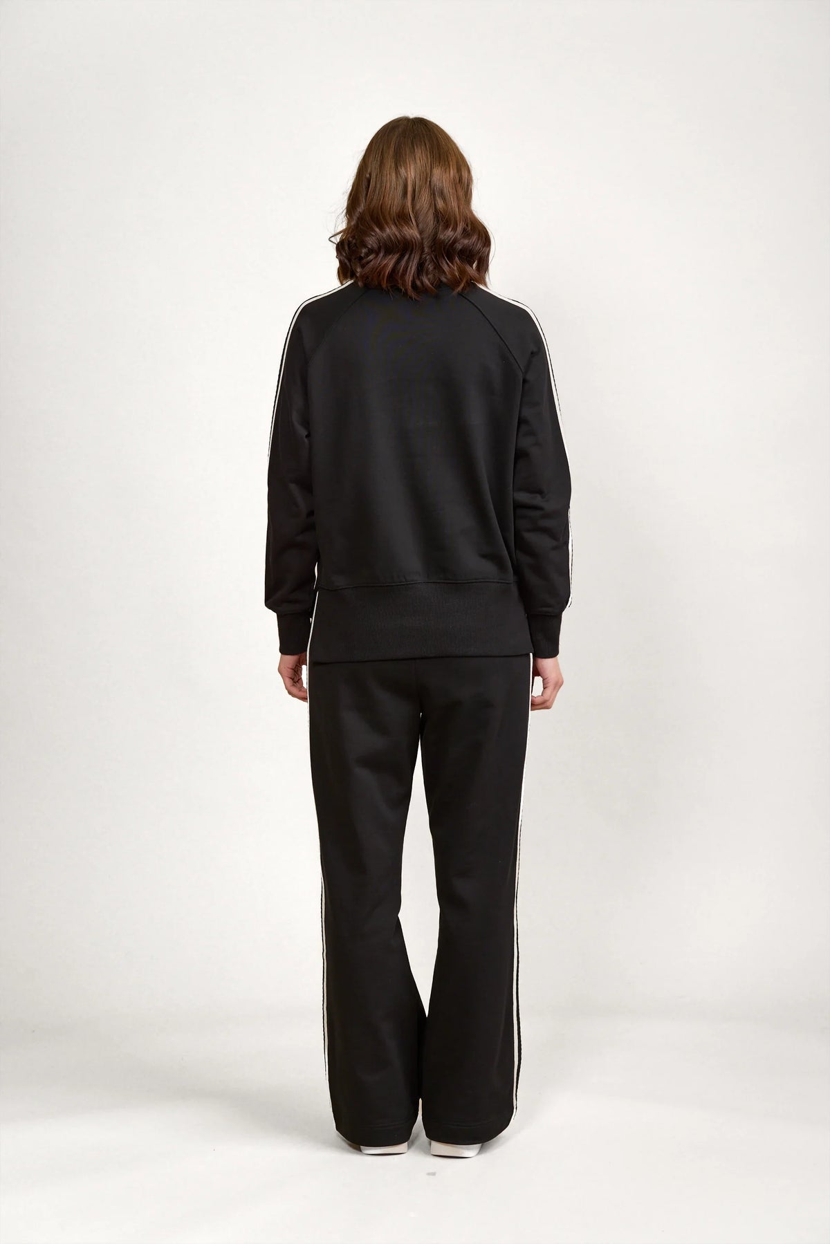 Back view of a woman wearing a black jumper and black pants with white side stripes