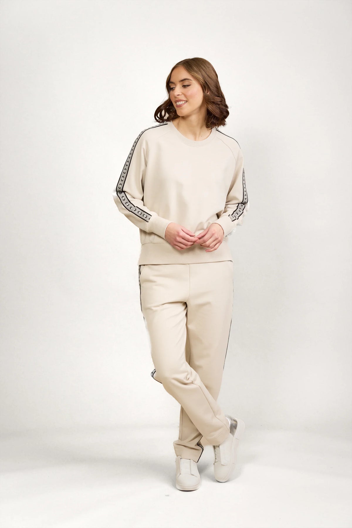 Woman wearing beige jumper and matching pants with black side stripe detail, white sneakers