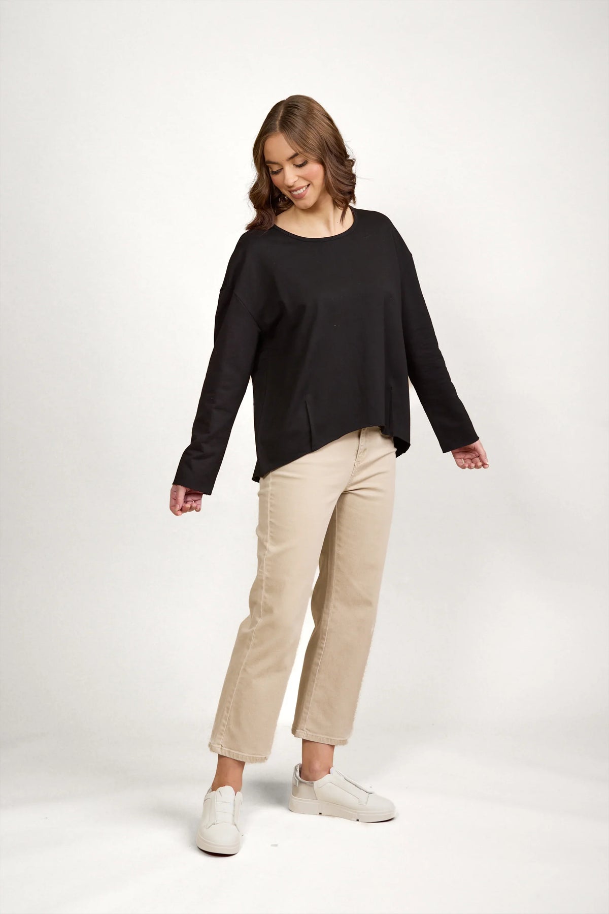 Woman in black long sleeve top with drop shoulders, beige wide-leg pants and white sneakers
