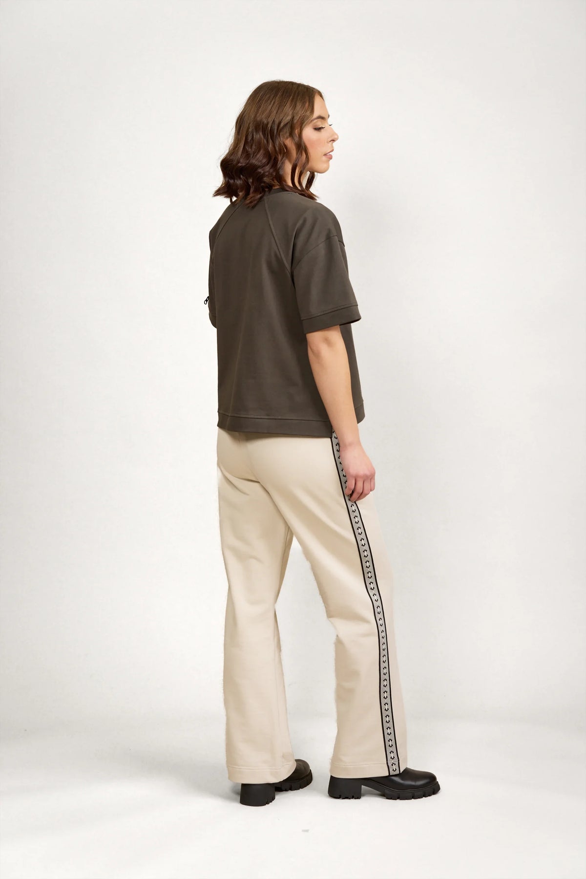 Woman wearing oversized khaki tee and cream track pants with logo side stripe in studio