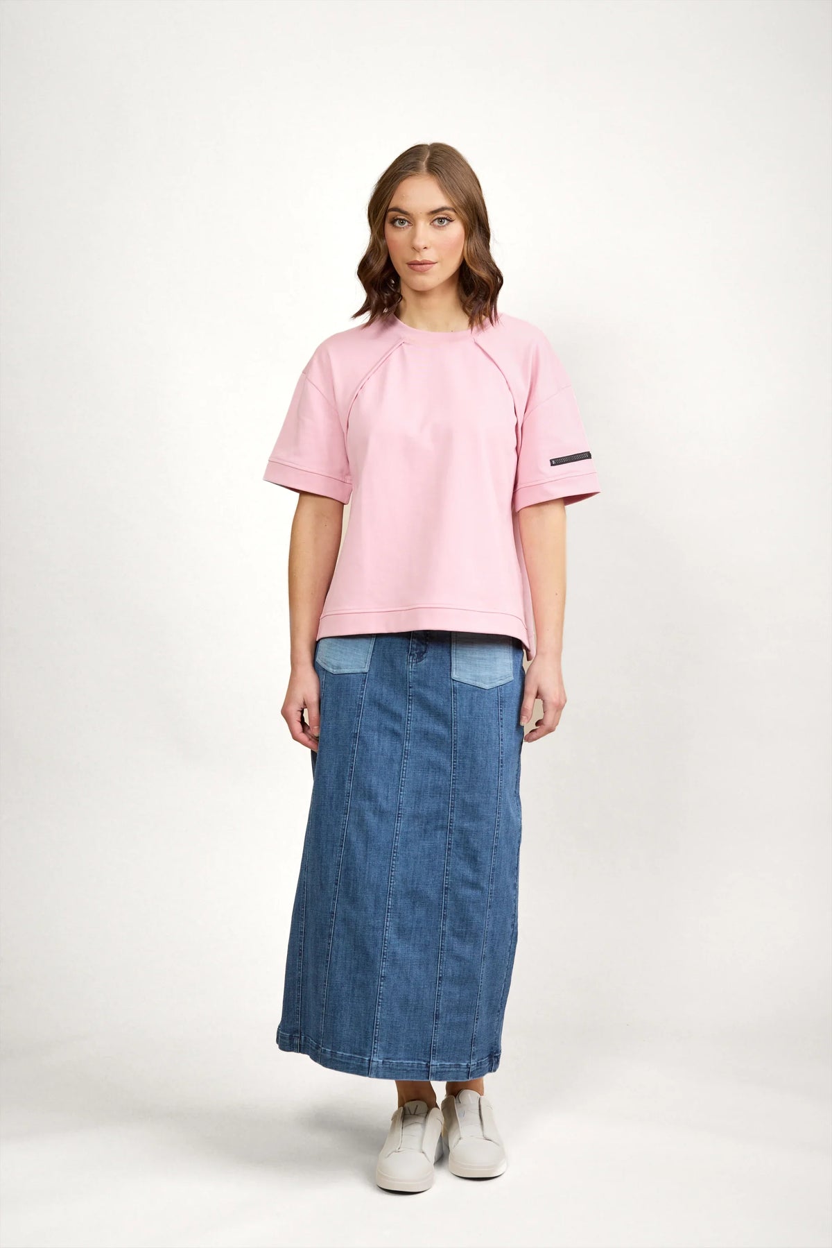 Woman wearing a pink short sleeve tee with patch detail and a denim maxi skirt, white sneakers