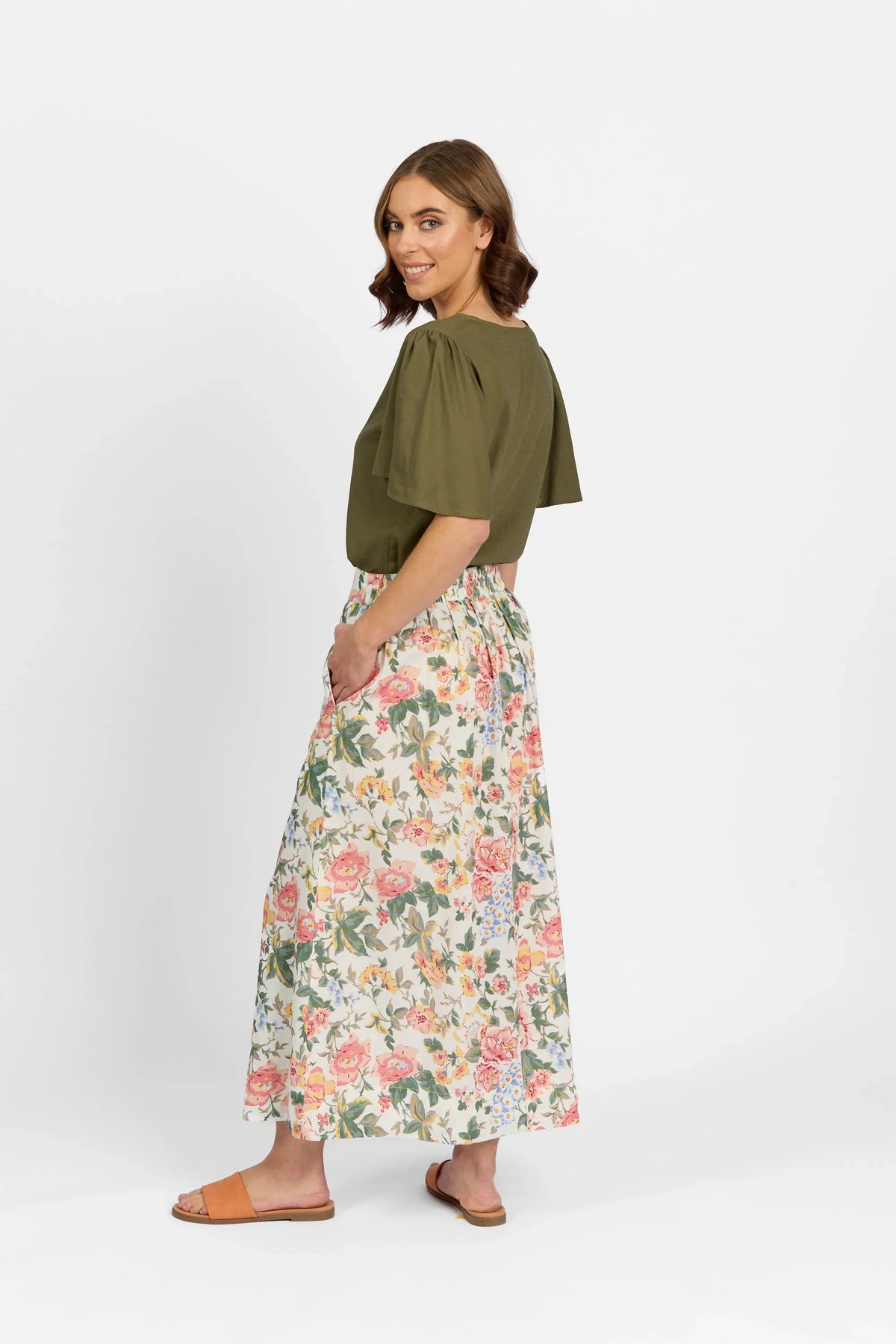 Woman in olive green blouse and floral maxi skirt with pockets, side view, white background