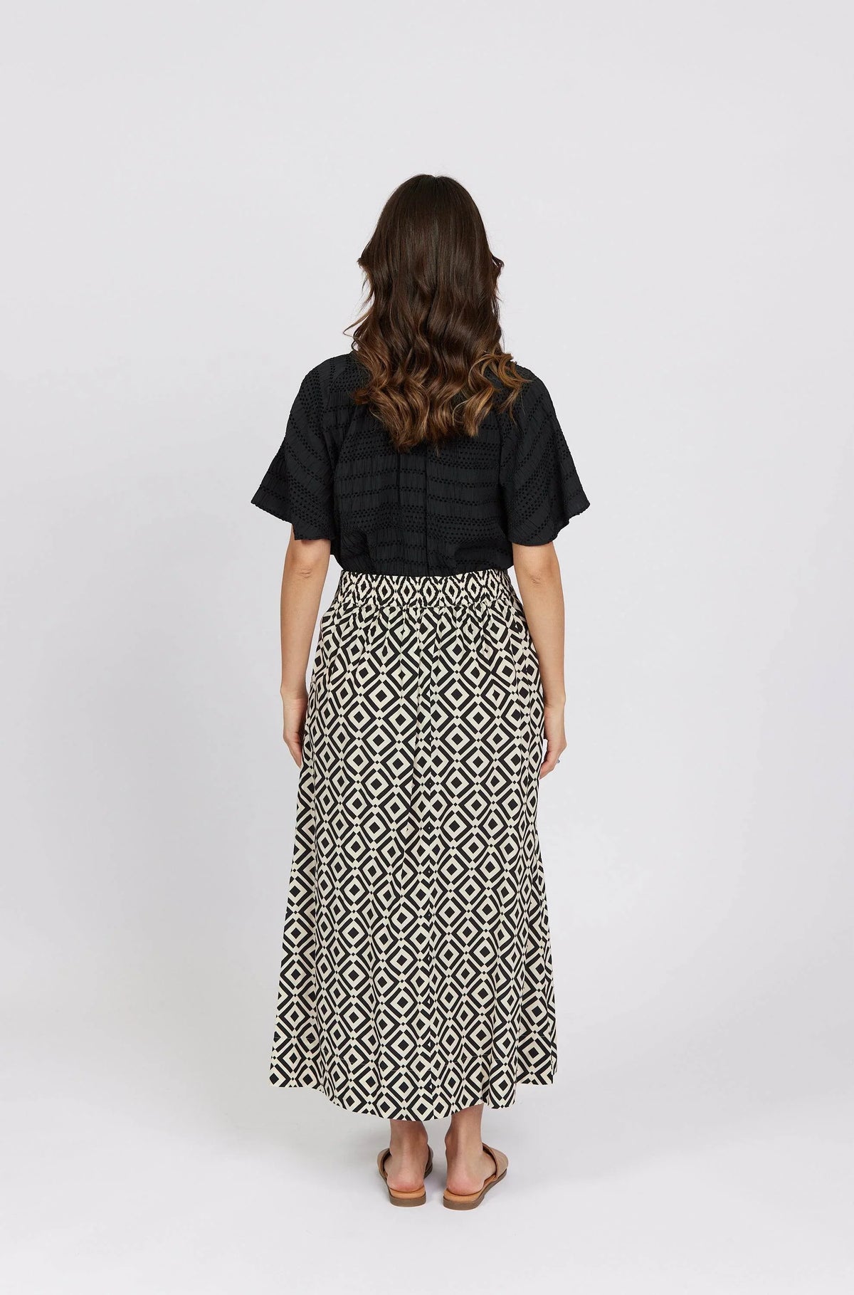 Woman wearing black top and geometric print maxi skirt, back view, studio setting