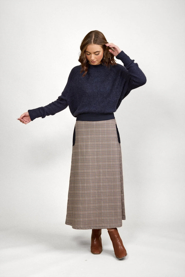 Woman in navy knit sweater and brown check A-line midi skirt with ankle boots on white background