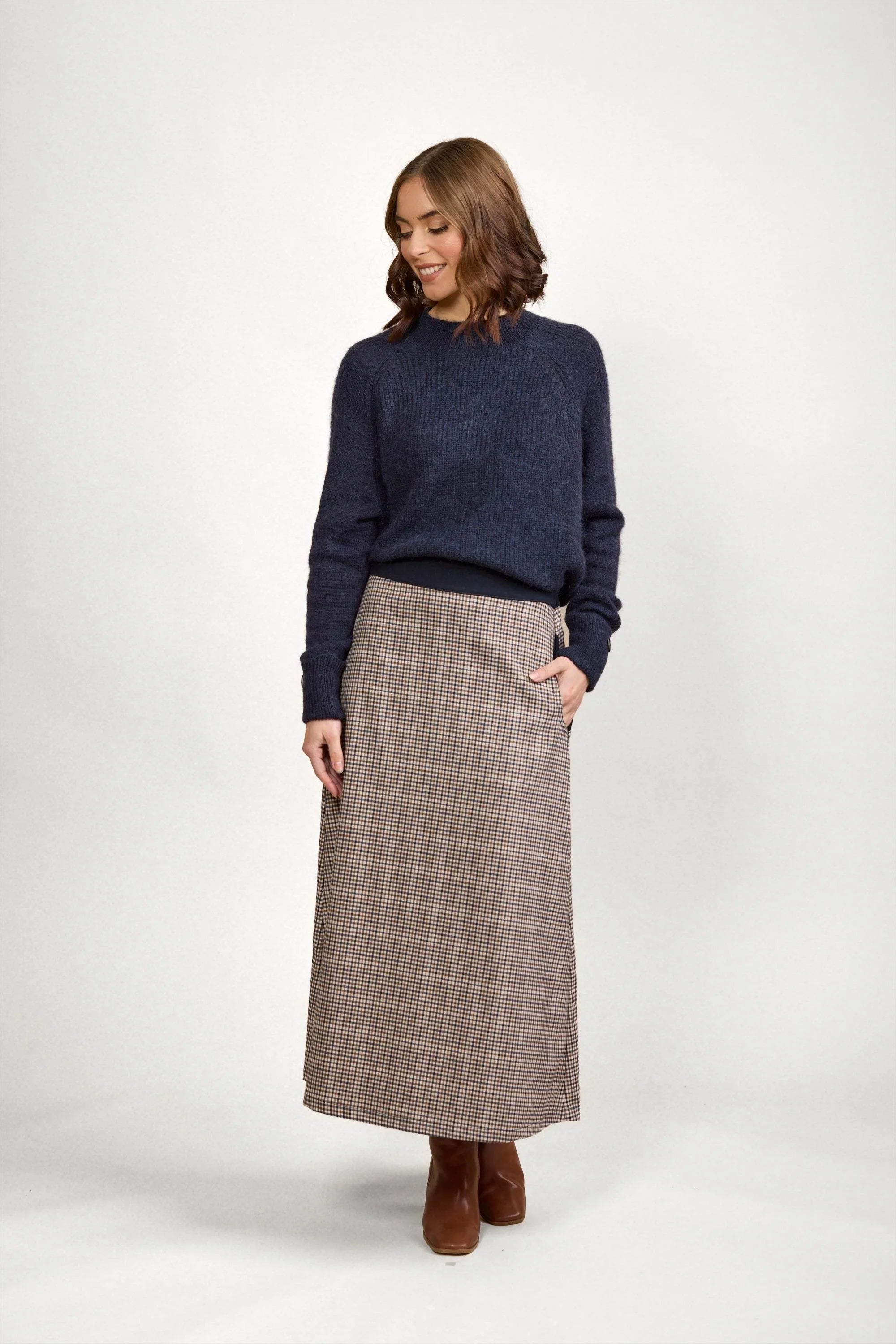 Woman wearing a navy knit sweater and checked maxi skirt with brown boots in studio